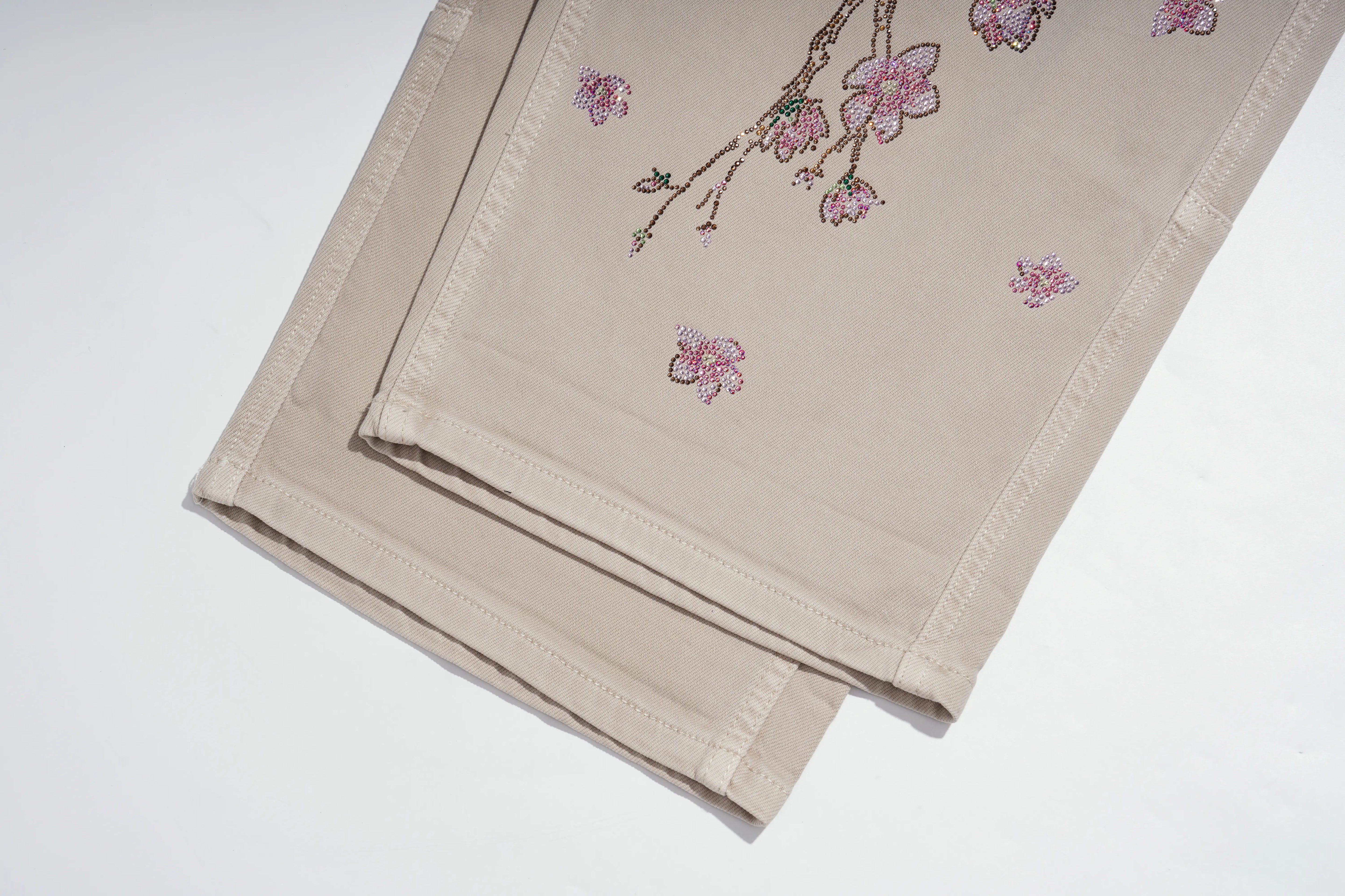 A folded beige fabric napkin or table linen with pink cherry blossom embroidery, displayed on a clean white background. TCH Rhinestone Cherry Blossom Straight-Leg Jeans