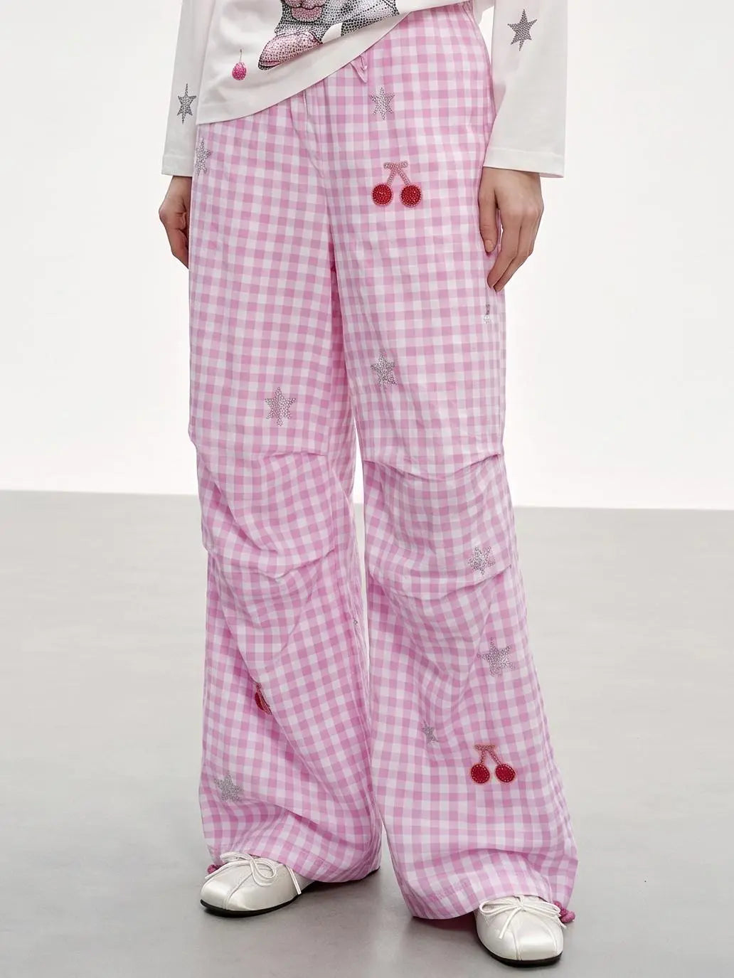 Pink and white gingham wide-leg pants with cherry and star embroidery, shown on a model wearing white shoes against a light gray studio background. TCH Rhinestone Cherry Gingham Cargo Wide-Leg Pants