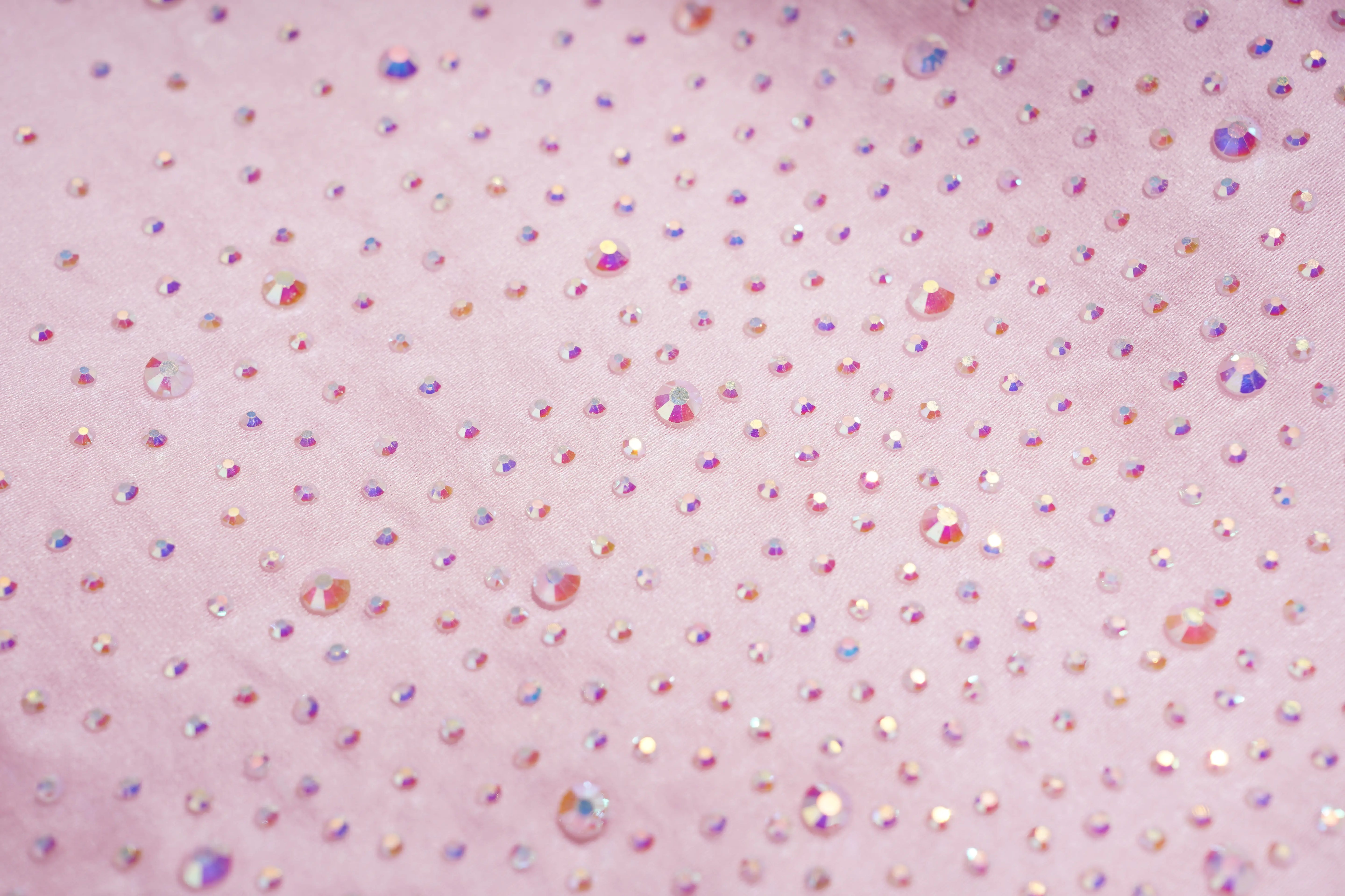 A close-up of a light pink fabric surface covered with many small iridescent rhinestones that reflect pink, purple, blue, and gold tones. TCH Rhinestone Crystal Embellished Pink Shirt & Shorts Set