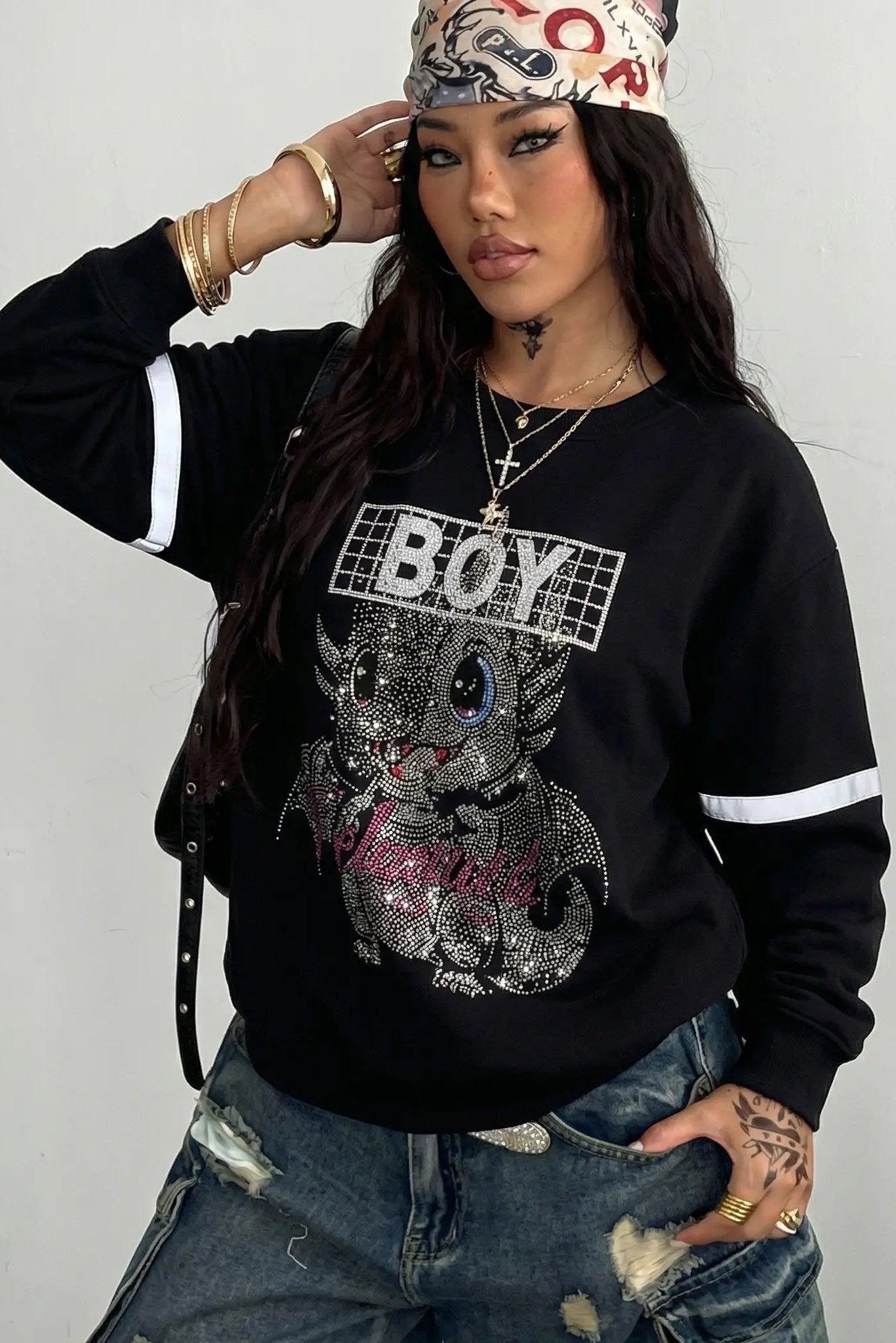 Person wearing a black sweatshirt with a cat graphic and 'BOY' text, paired with ripped jeans and a headband. TCH Rhinestone Cute Dragon Sweatshirt