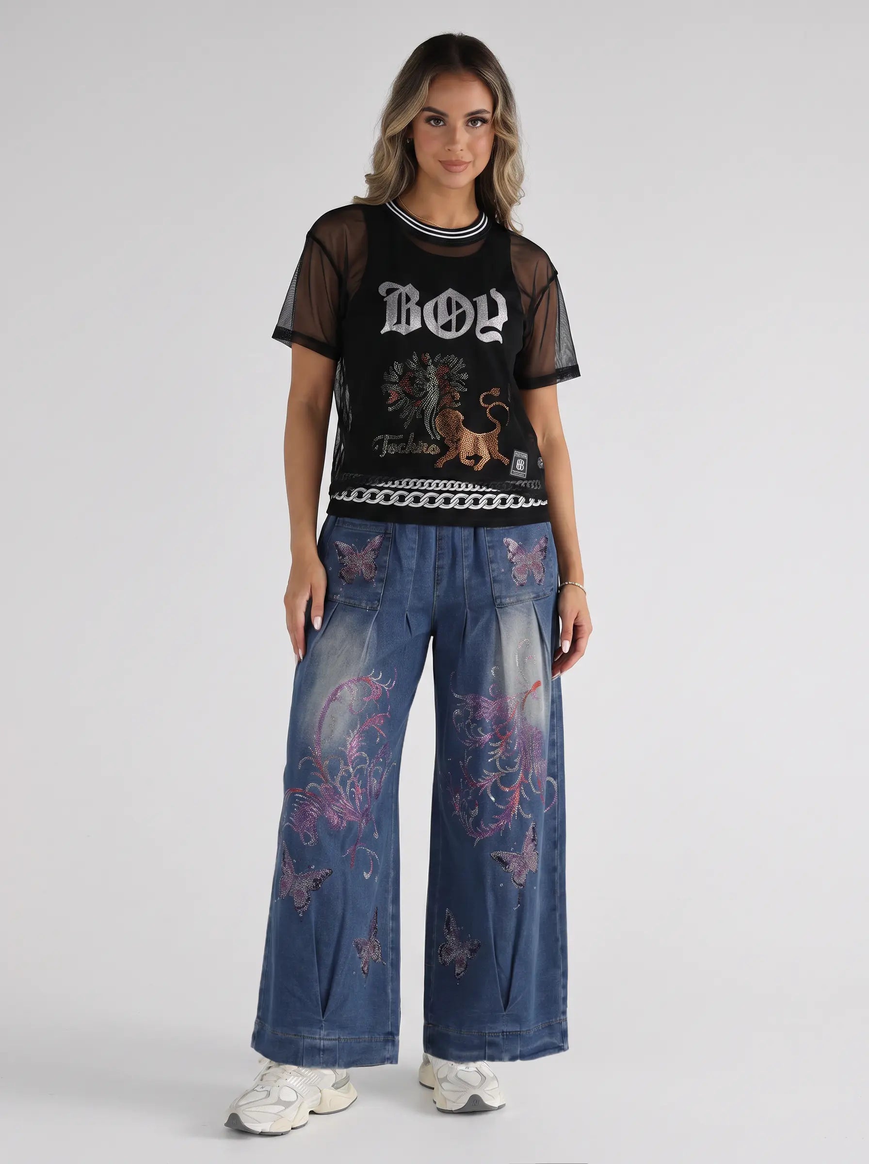 A model stands against a light gray studio background wearing a black short-sleeve graphic T-shirt with sheer sleeves and a white 'BOY' logo, paired with wide-leg blue jeans featuring pink and purple dragon prints, and white sneakers. TCH Rhinestone Deer Graphic Mesh Sleeve Black Streetwear T-Shirt