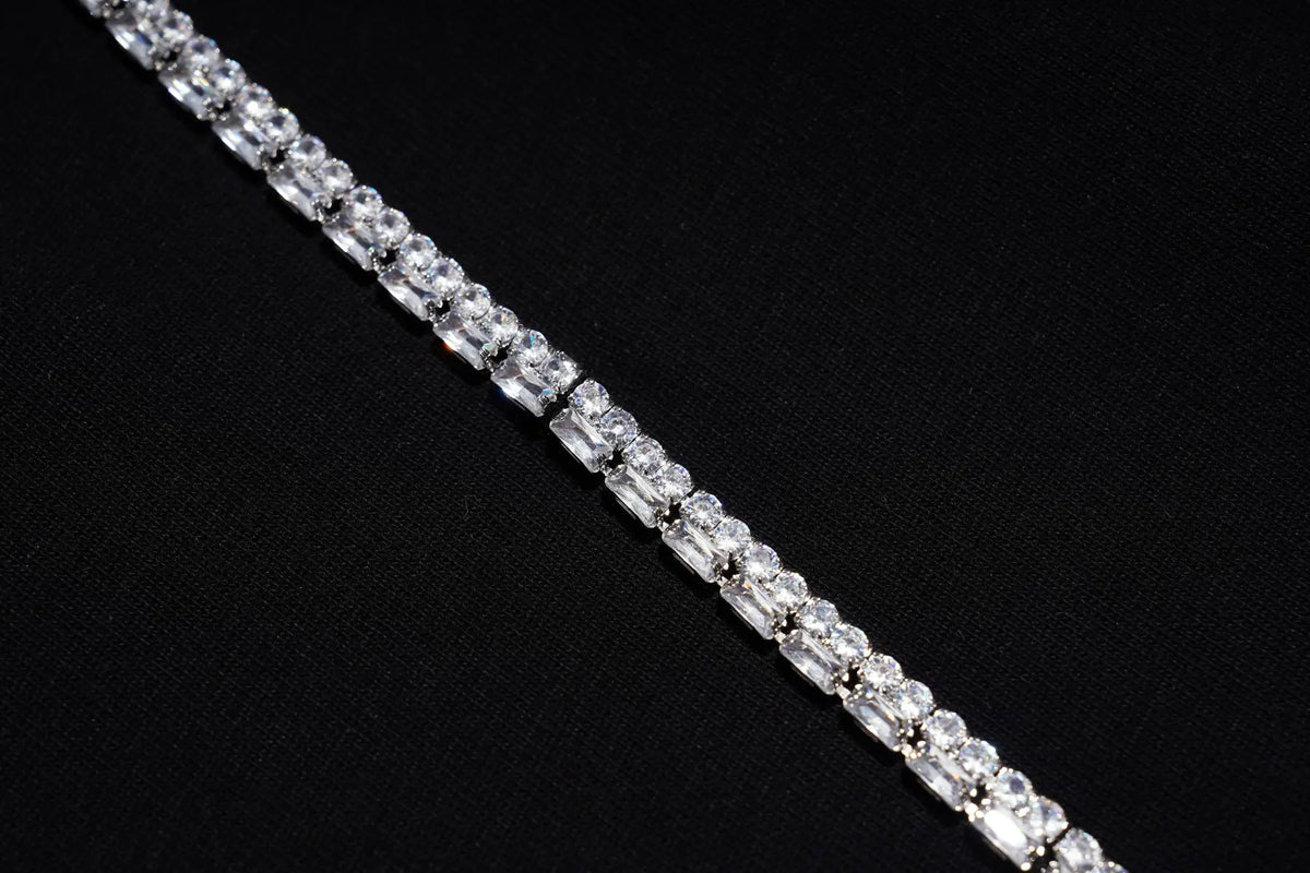 A close-up of a silver tennis bracelet set with clear rectangular-cut stones, laid diagonally on a textured black background. TCH Rhinestone Denim Corset Graphic Oversized T-Shirt