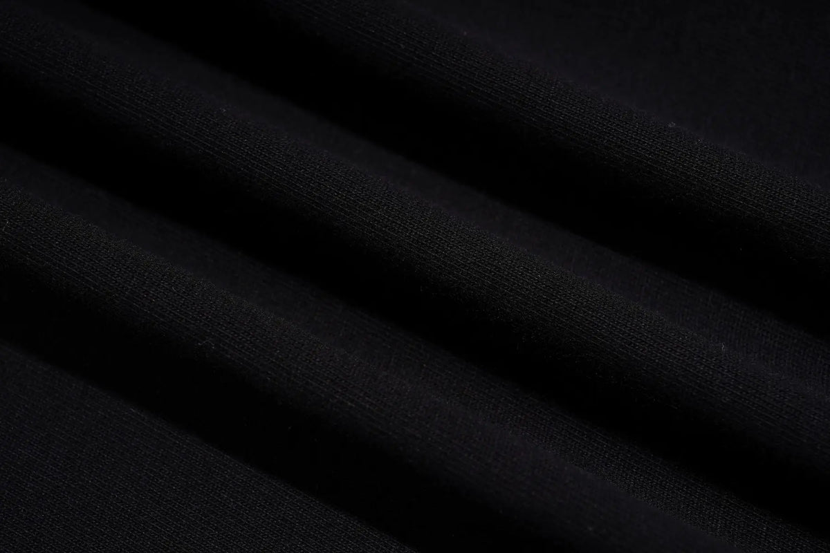 A close-up of draped black fabric with soft diagonal folds showing a fine knit texture. TCH Rhinestone Denim Corset Graphic Oversized T-Shirt