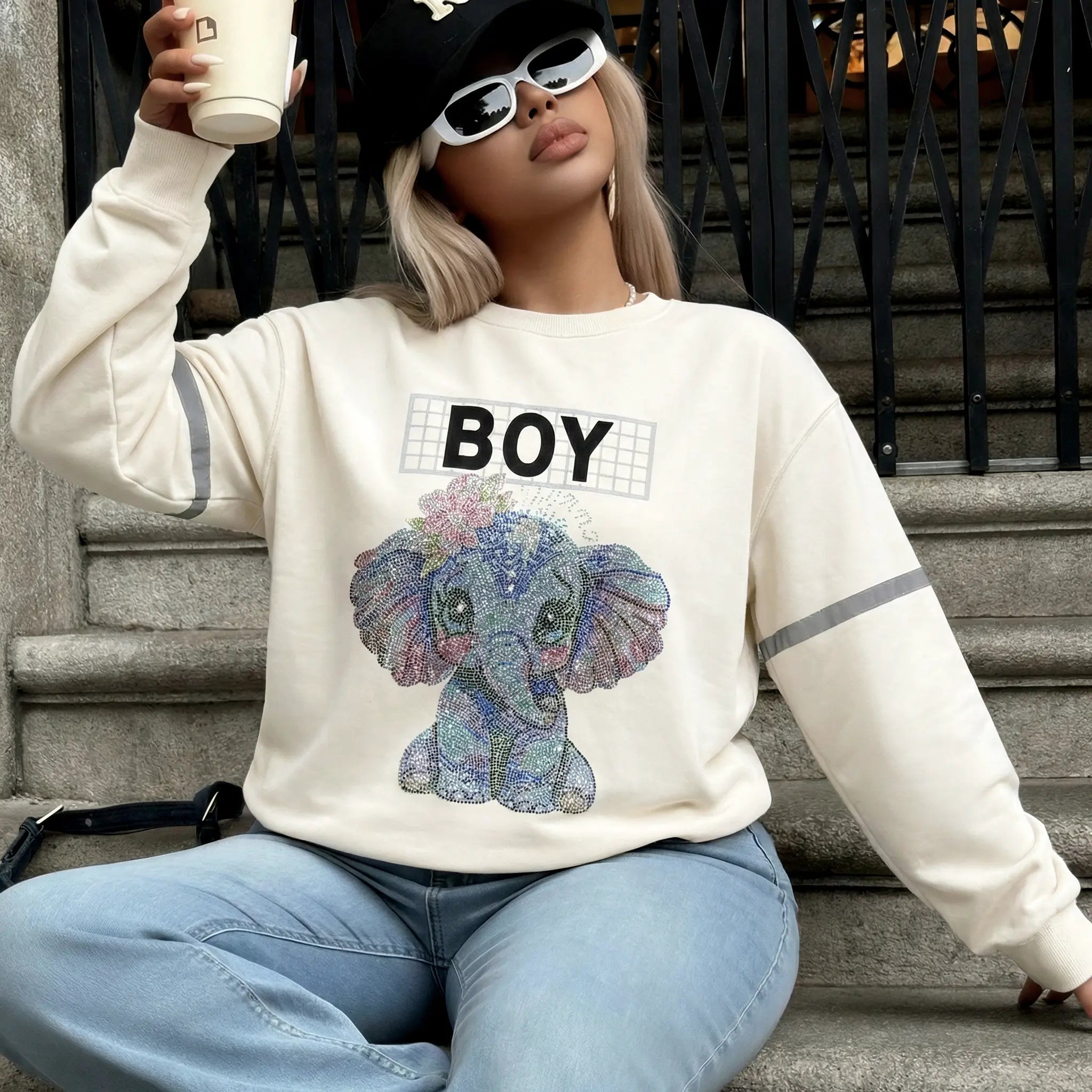 Person wearing a sweatshirt with an elephant graphic and 'BOY' text, sitting on steps. TCH Rhinestone Elephant Graphic Crew Neck Sweatshirt