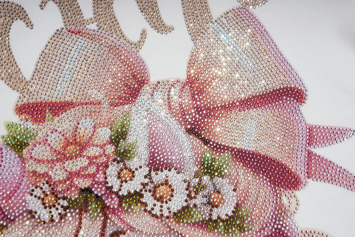A close-up of a pink rhinestone-style decorative bow with floral embellishments and metallic gold curved accents on a white background. TCH Rhinestone Fantasy Unicorn Graphic Long Sleeve T-Shirt