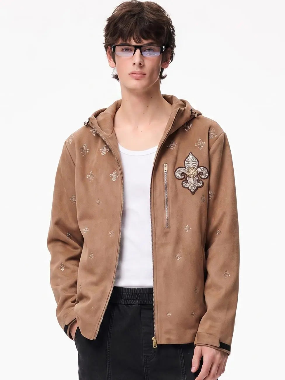 A young man wearing a tan suede zip-up hoodie with a fleur-de-lis patch on the chest, styled over a white t-shirt and black pants, photographed against a plain white background. TCH Rhinestone Fleur-de-Lis Hooded Jacket
