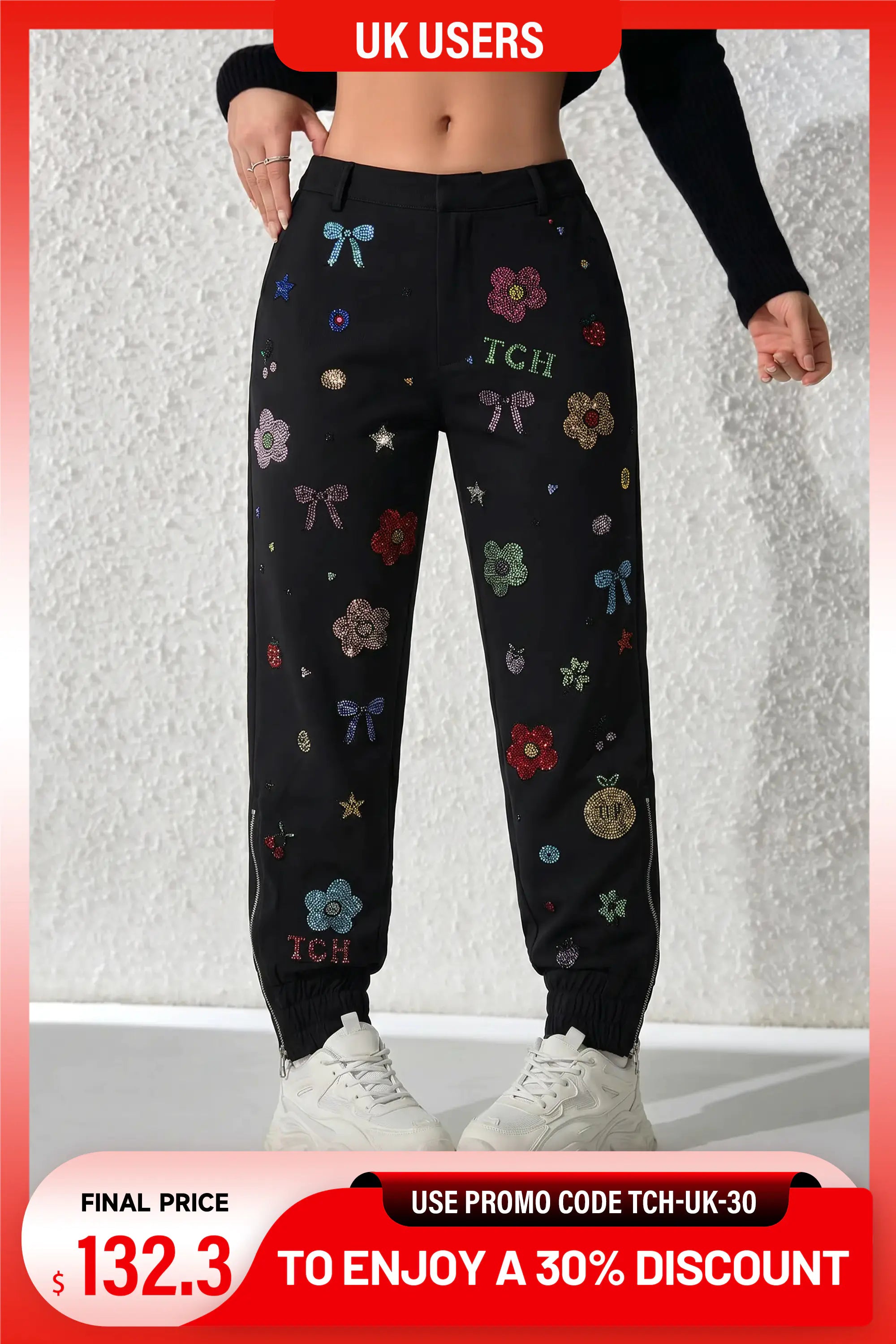 Black jogger sweatpants with colorful embroidered bows, flowers, stars, and 'TCH' lettering, shown on a model from the waist down against a textured white wall. TCH Rhinestone Floral Jogger Pants – Black Streetwear Edition
