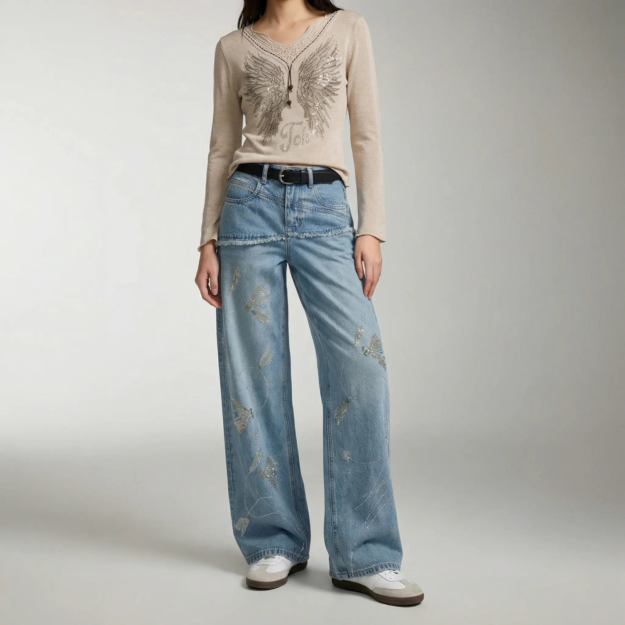 Person wearing a beige sweater with a decorative pattern and light blue jeans on a plain background, TCH Rhinestone Floral Wide-Leg Blue Jeans