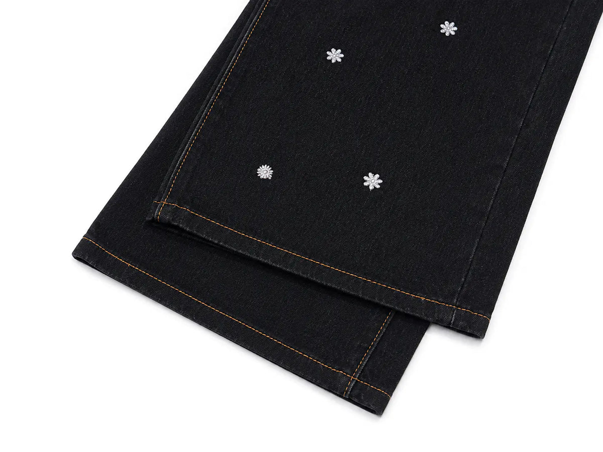Close-up of folded black denim jeans on a white background, showing orange contrast stitching and small white embroidered flower motifs. TCH Rhinestone Floral Wide-Leg Jeans