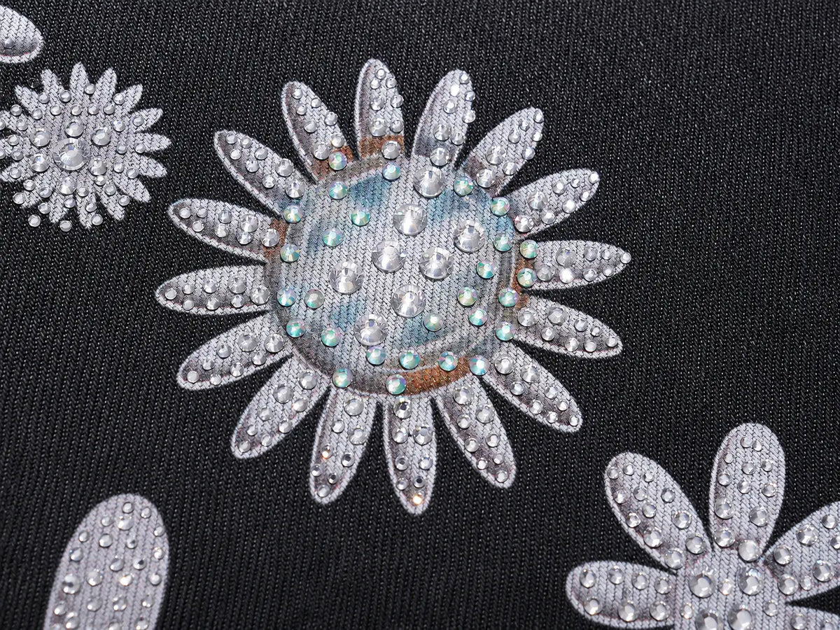 Close-up of a black fabric garment featuring large silver-gray embroidered daisy flowers embellished with clear rhinestones and iridescent blue-green accents. TCH Rhinestone Floral Wide-Leg Jeans