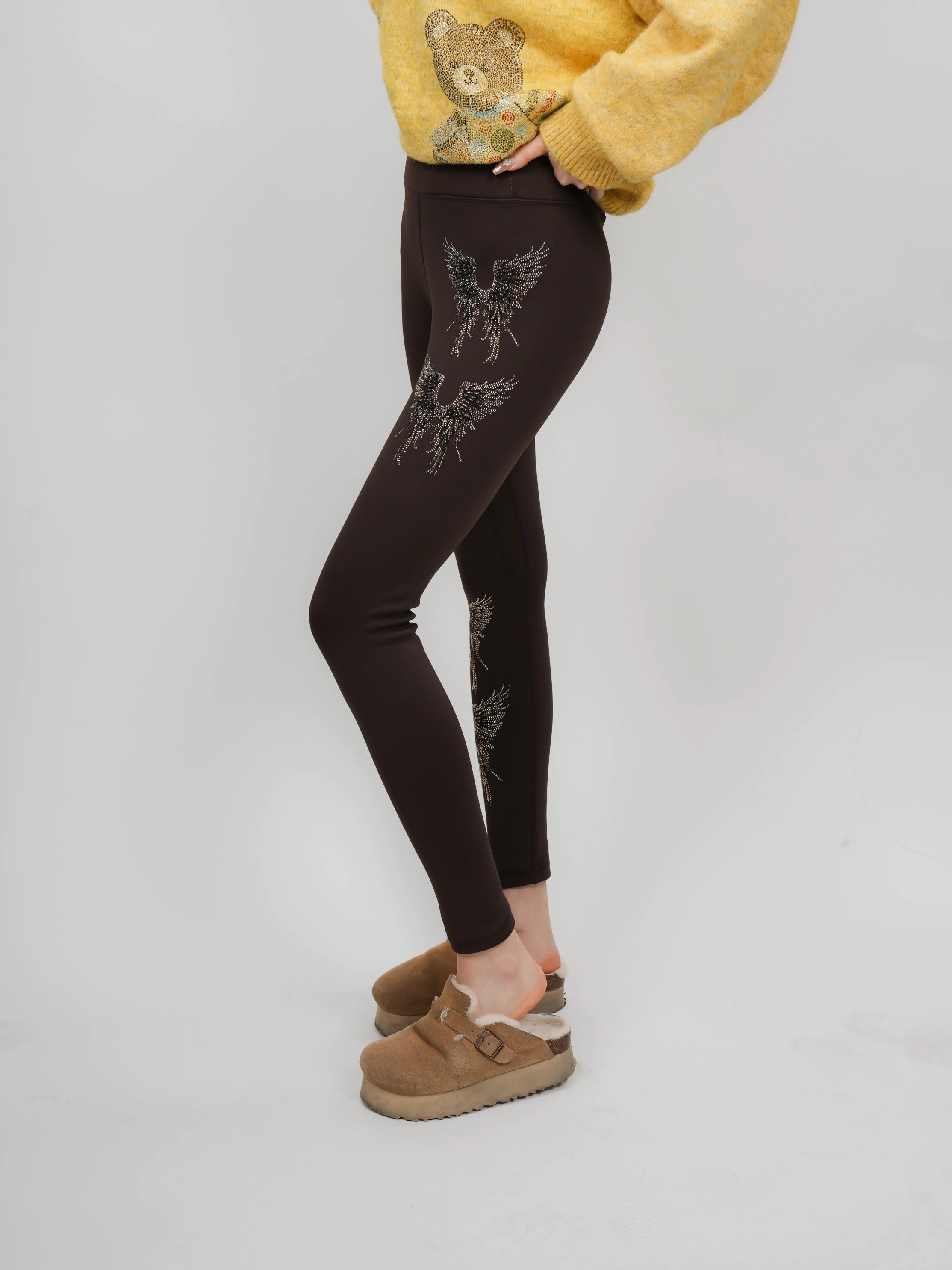 Person wearing brown leggings with floral patterns on a plain background, TCH Rhinestone Golden Wings Black High-Waist Leggings