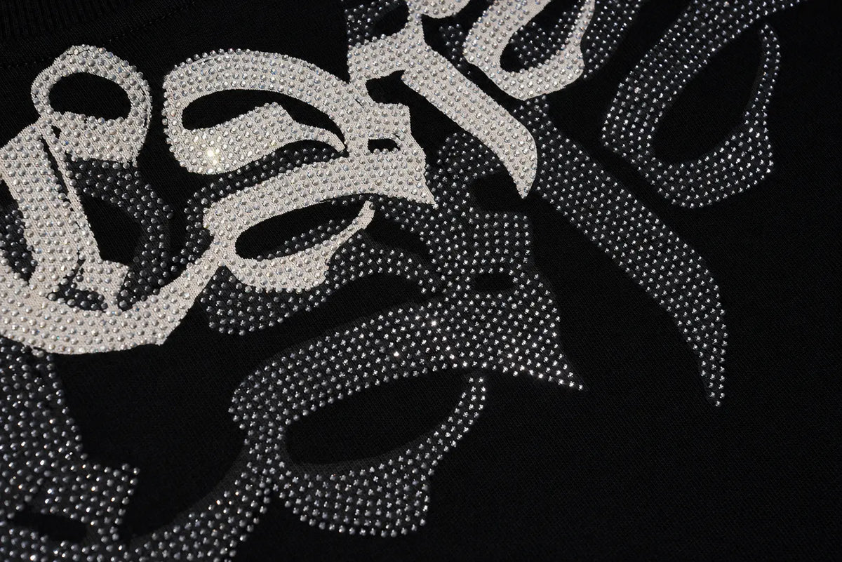 A close-up of a black garment featuring a large, stylized script graphic embellished with silver rhinestones, spelling out 'Batale'. TCH Rhinestone Graphic Black Crewneck Sweatshirt
