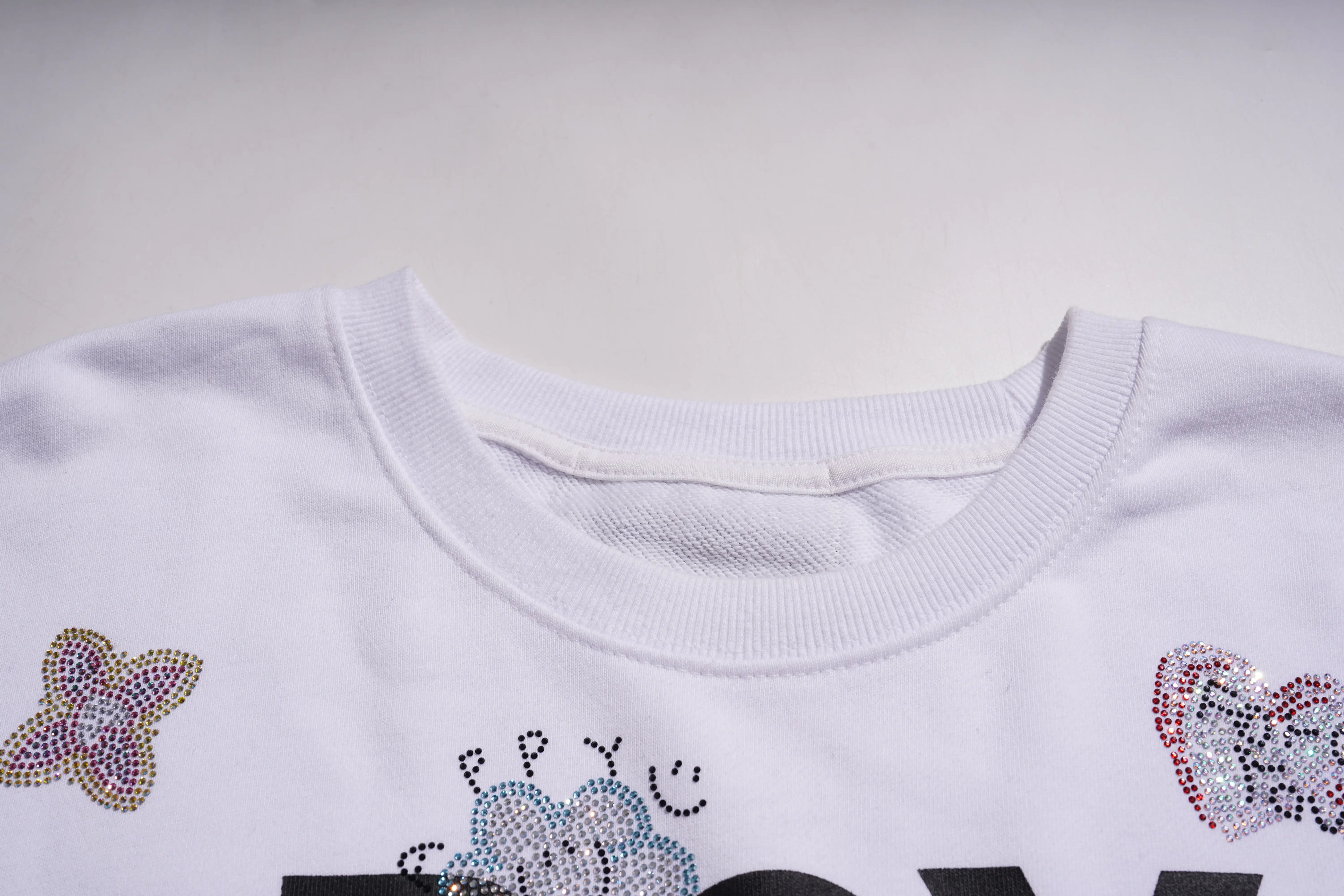 Close-up of a white shirt with decorative elements on a plain background, TCH Rhinestone Logo Print Crew Neck Sweatshirt