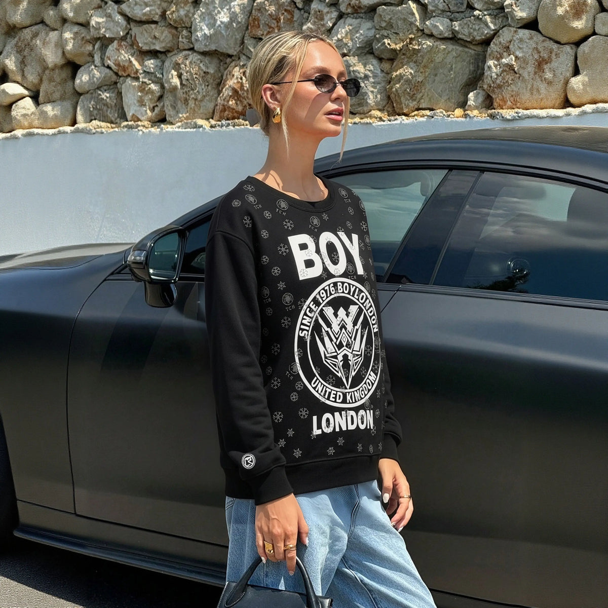 Person wearing a black sweatshirt with visible branding, standing next to a car. TCH Rhinestone Mech Logo Crew Neck Sweatshirt