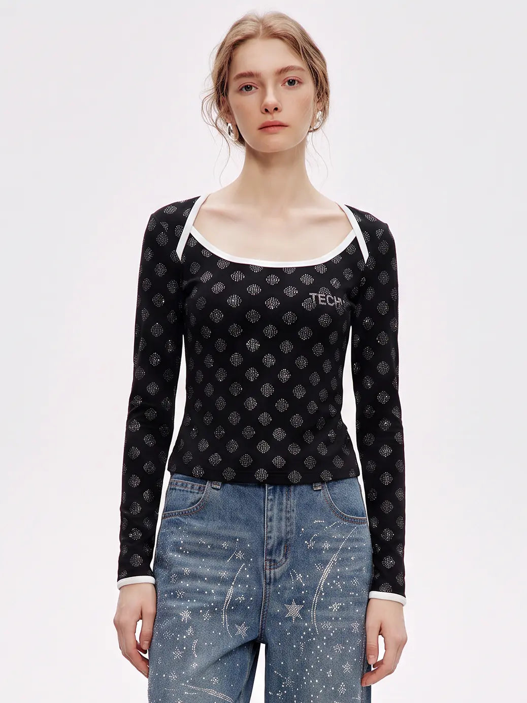 A model wearing a black long-sleeve scoop-neck top with a small gray geometric pattern and white trim, paired with blue jeans, against a plain white studio background. TCH Rhinestone Pattern Long Sleeve Top