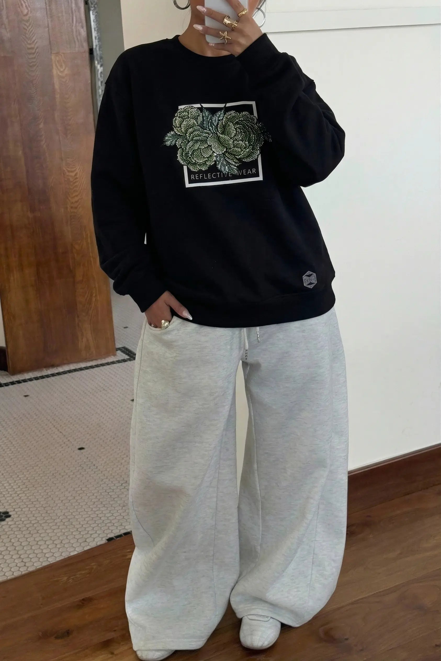 Person wearing a black sweatshirt with a succulent design and light gray pants indoors. TCH Rhinestone Peony Sweatshirt