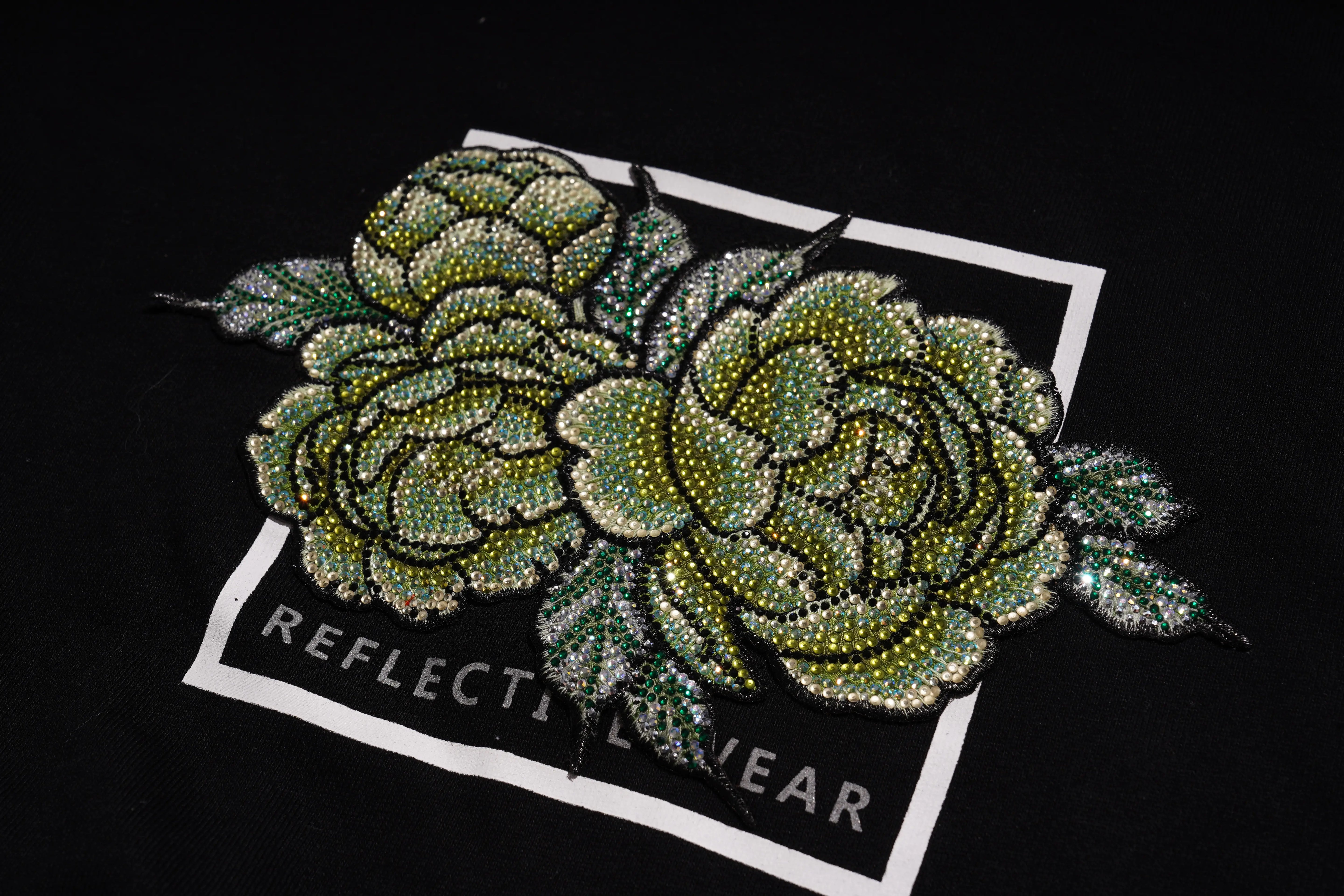 Decorative green flower patch with 'Reflective Wear' label on a black background, TCH Rhinestone Peony Sweatshirt