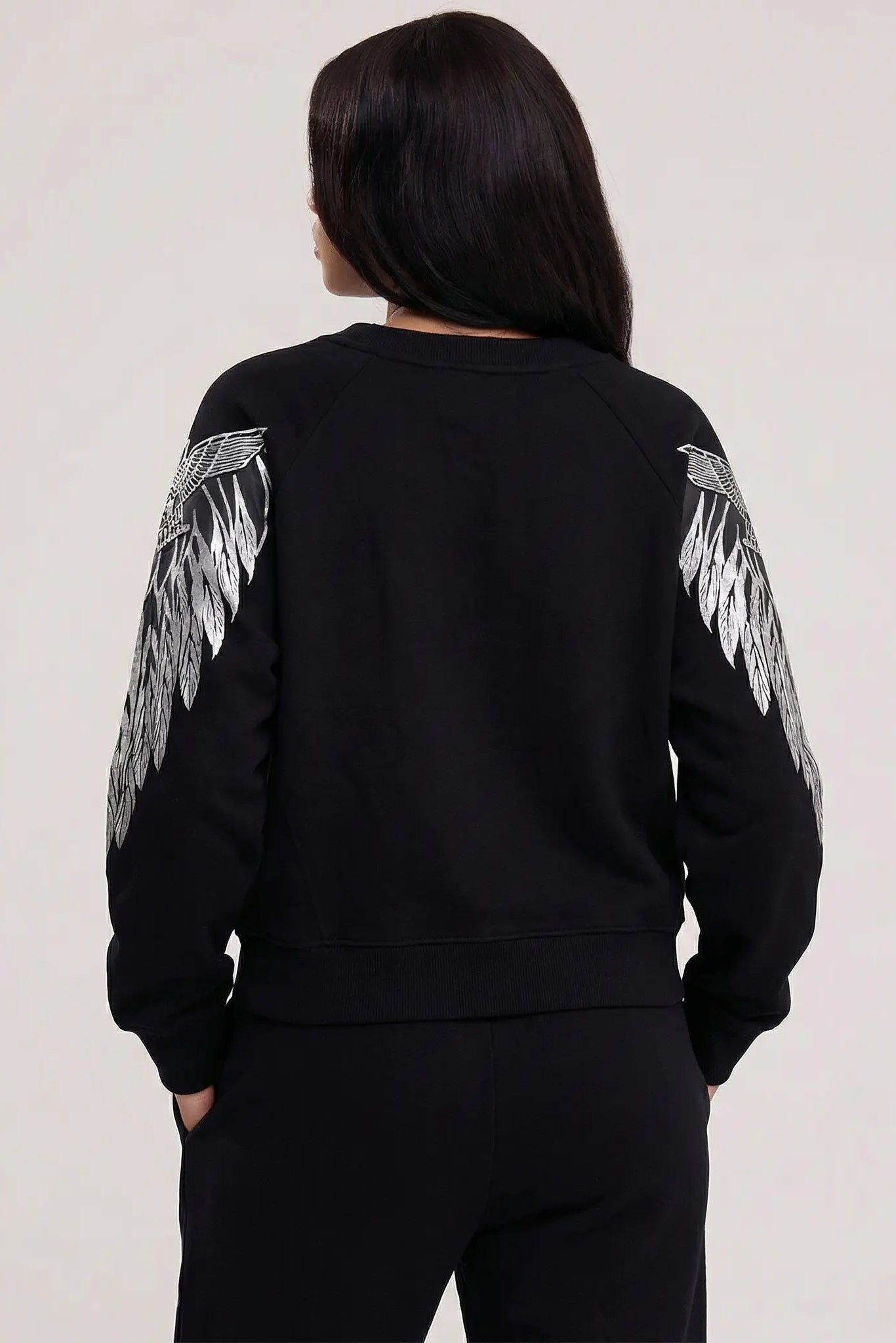 Person wearing a black sweatshirt with feather designs on sleeves against a plain background, TCH Rhinestone Peony Wing Graphic Crew Neck Sweatshirt