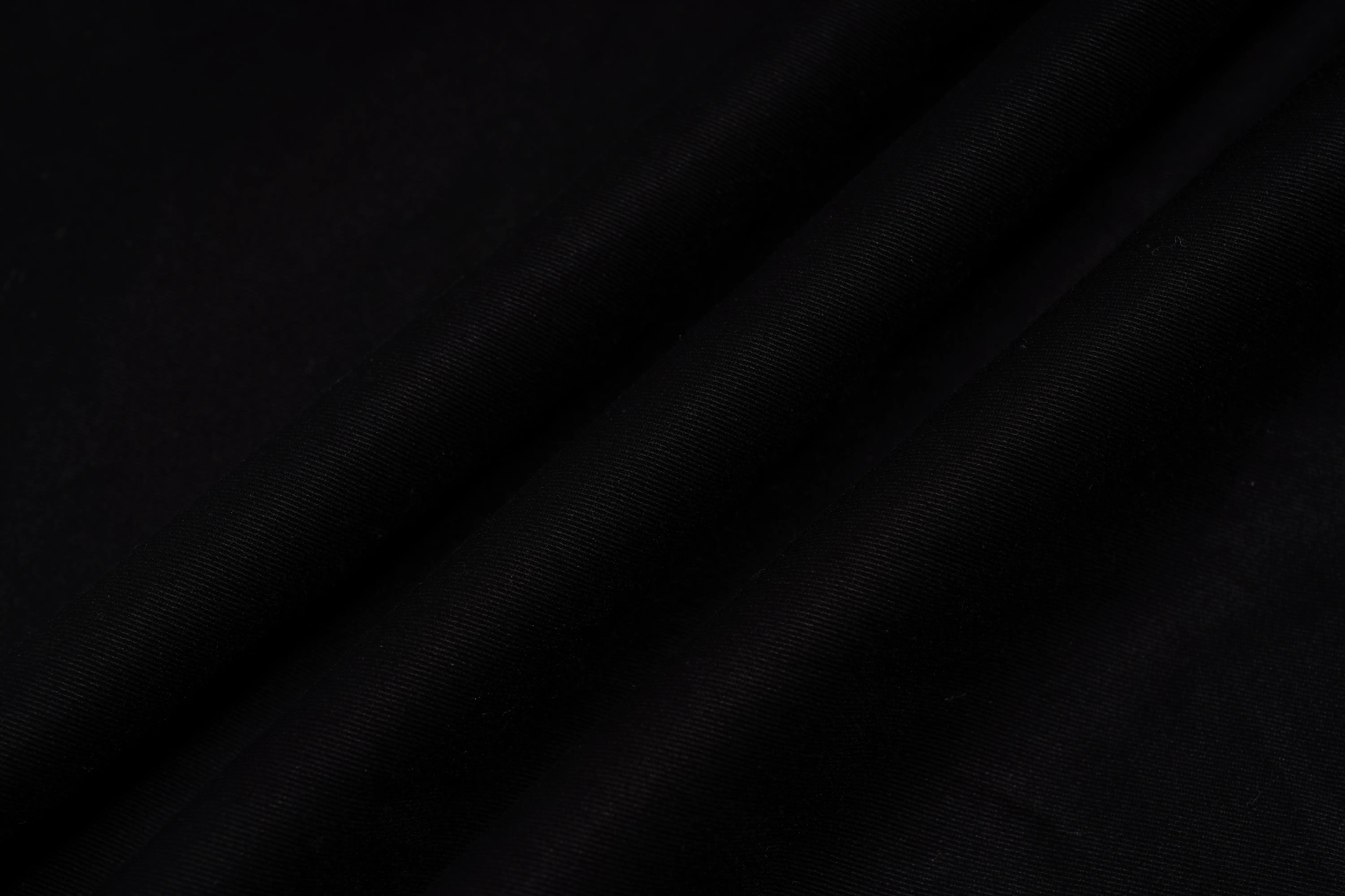 A close-up of draped black fabric with soft folds and a smooth texture. TCH Rhinestone Phoenix Cargo Wide-Leg Pants