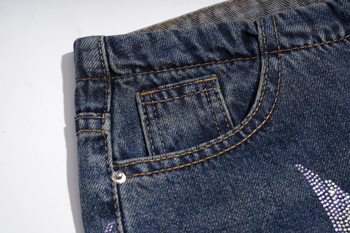 Close-up of the back pocket area of dark blue denim jeans, showing tan contrast stitching, a silver rivet, and a rhinestone-embellished detail on the leg. TCH Rhinestone Phoenix Wide-Leg Jeans