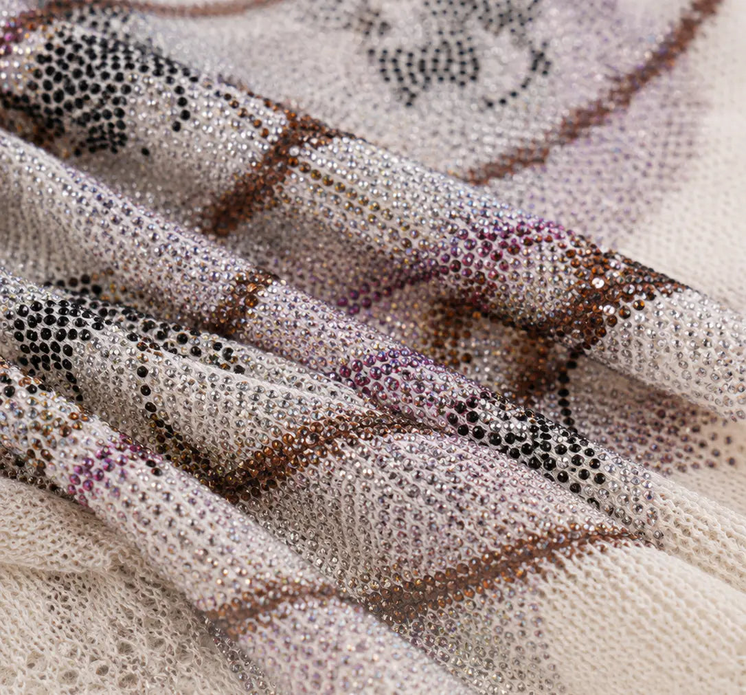 A close-up of a sheer mesh fabric with a dense beaded pattern in silver, black, brown, and purple, draped in soft folds. TCH Rhinestone Piggy Bow Striped Knit Top
