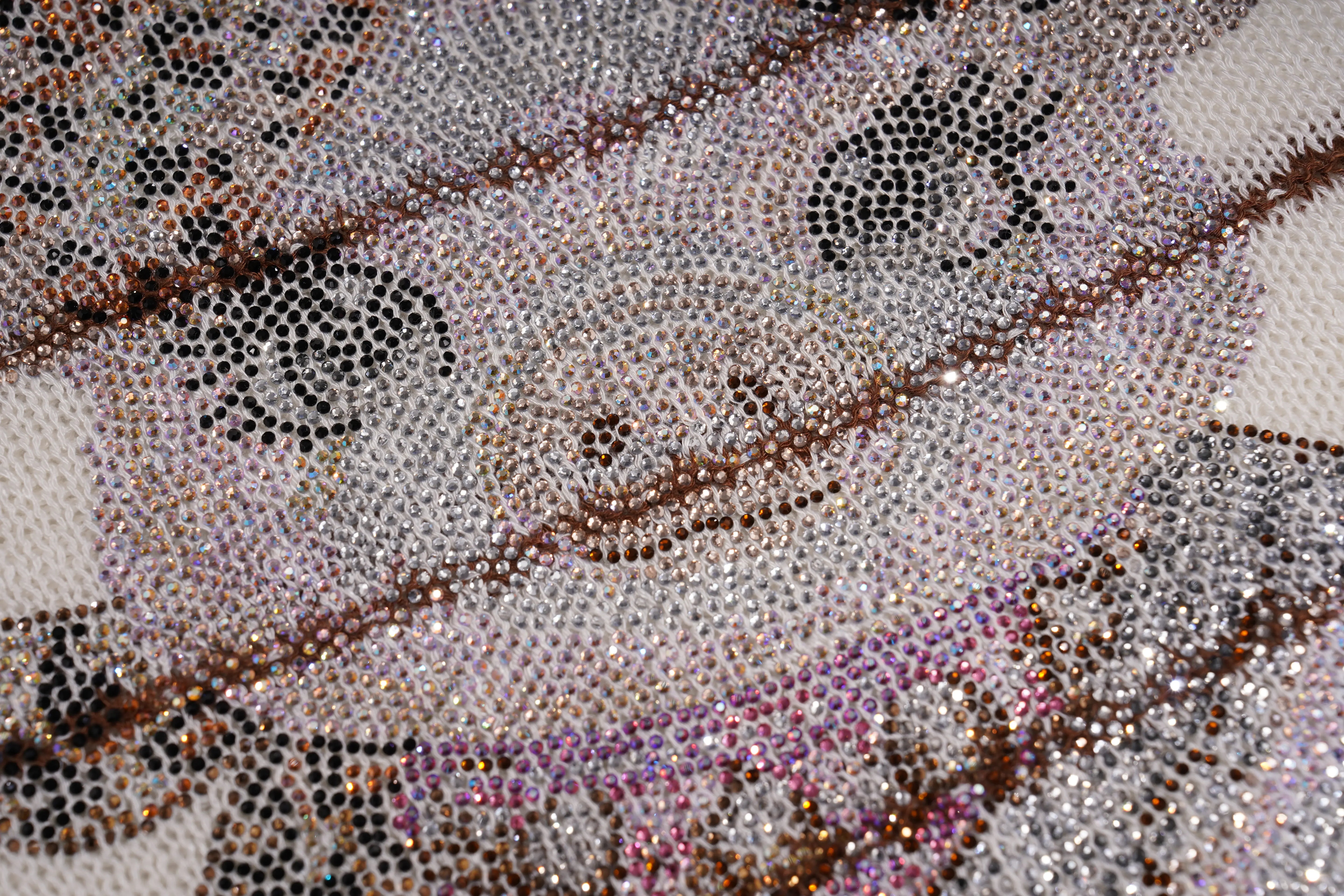 Close-up of a beaded textile or fabric pattern featuring a stylized face, composed of silver, black, brown, and iridescent rhinestones on a white mesh backing. TCH Rhinestone Piggy Bow Striped Knit Top
