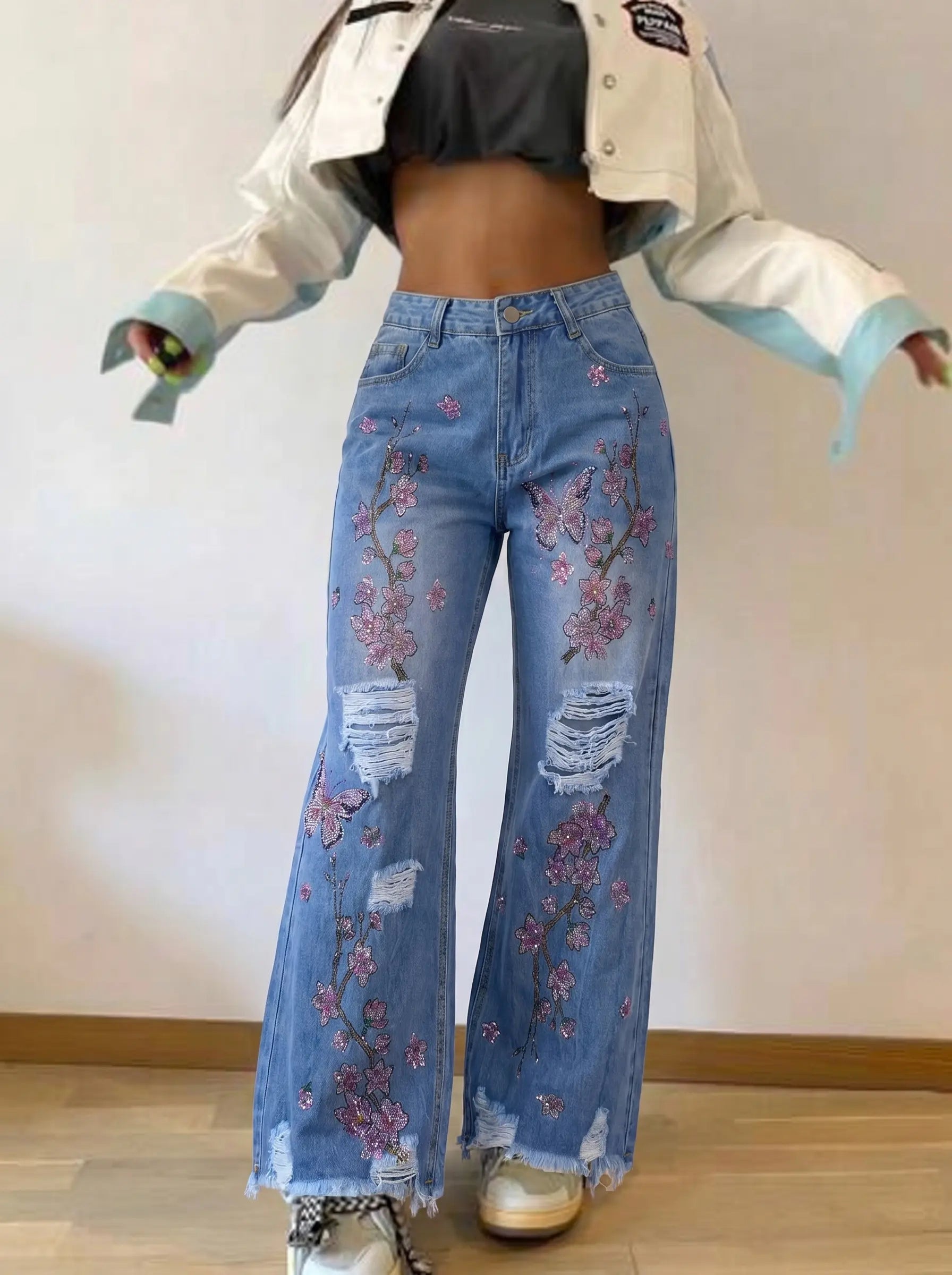 Person wearing floral embroidered jeans with a light jacket and black top indoors. TCH Rhinestone Plum Blossom Tree Distressed Denim Jeans