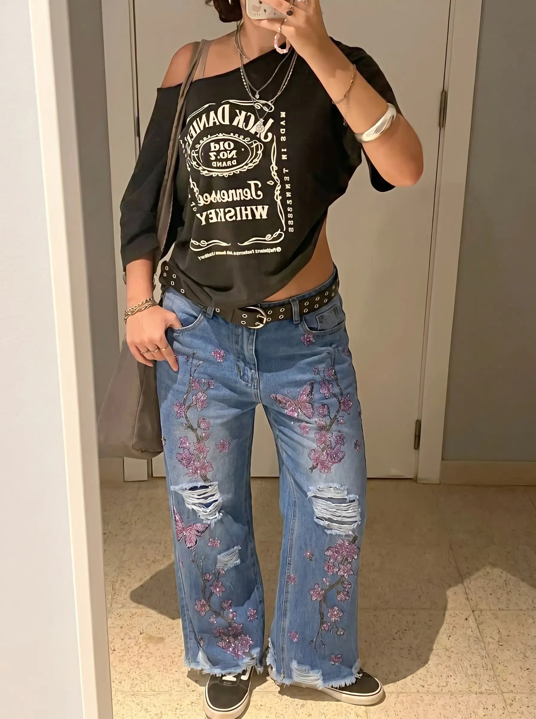 Person wearing a black graphic t-shirt and floral jeans in a room. TCH Rhinestone Plum Blossom Tree Distressed Denim Jeans