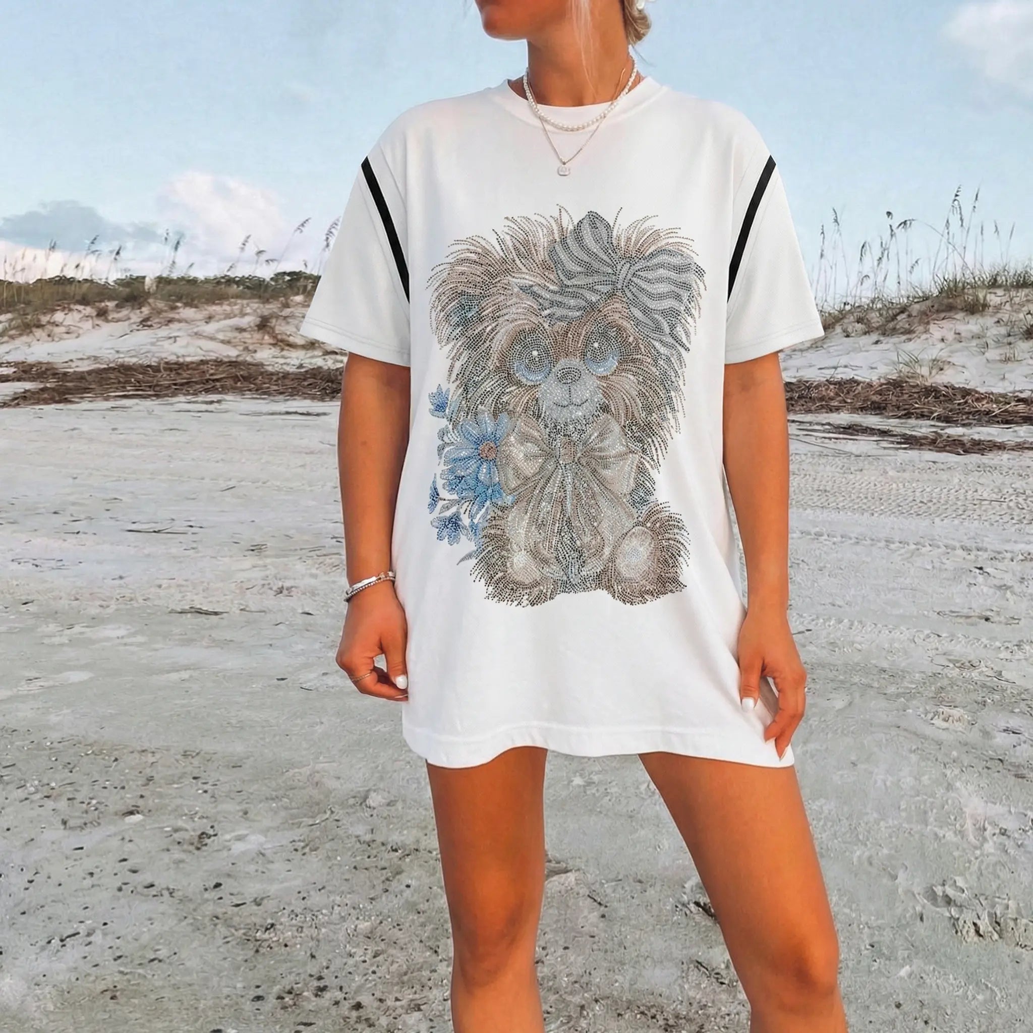 Person wearing a white t-shirt with a dog graphic on a sandy beach. TCH Rhinestone Puppy Bow White T-Shirt-1