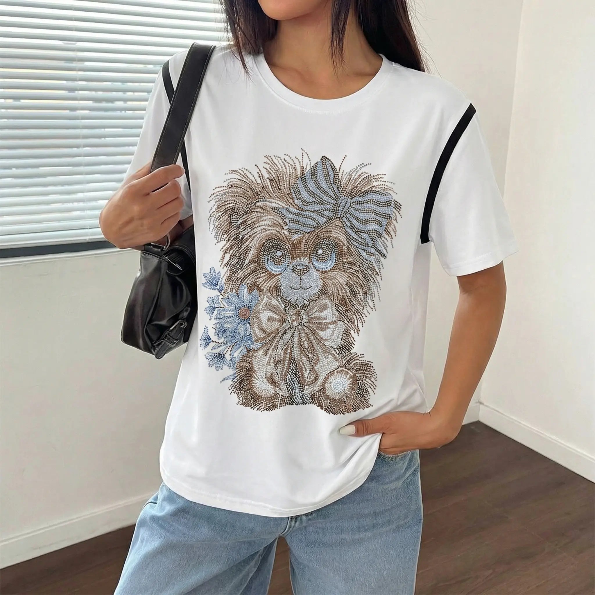 Person wearing a white t-shirt with a dog graphic design, holding a black bag. TCH Rhinestone Puppy Bow White T-Shirt-1