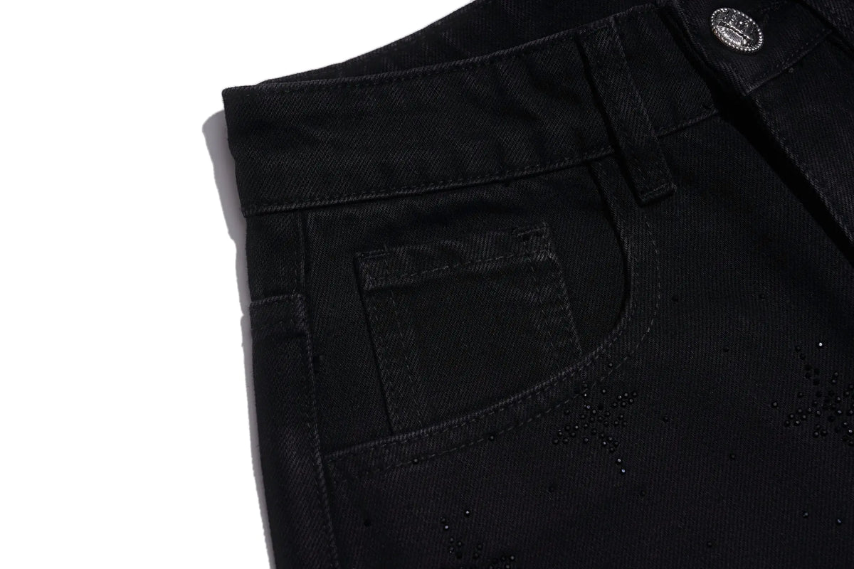 Close-up of a black denim garment, showing the back pocket, waistband, button, and small scattered dark embellishments on a white background. TCH Rhinestone Script Graphic Wide-Leg Jeans