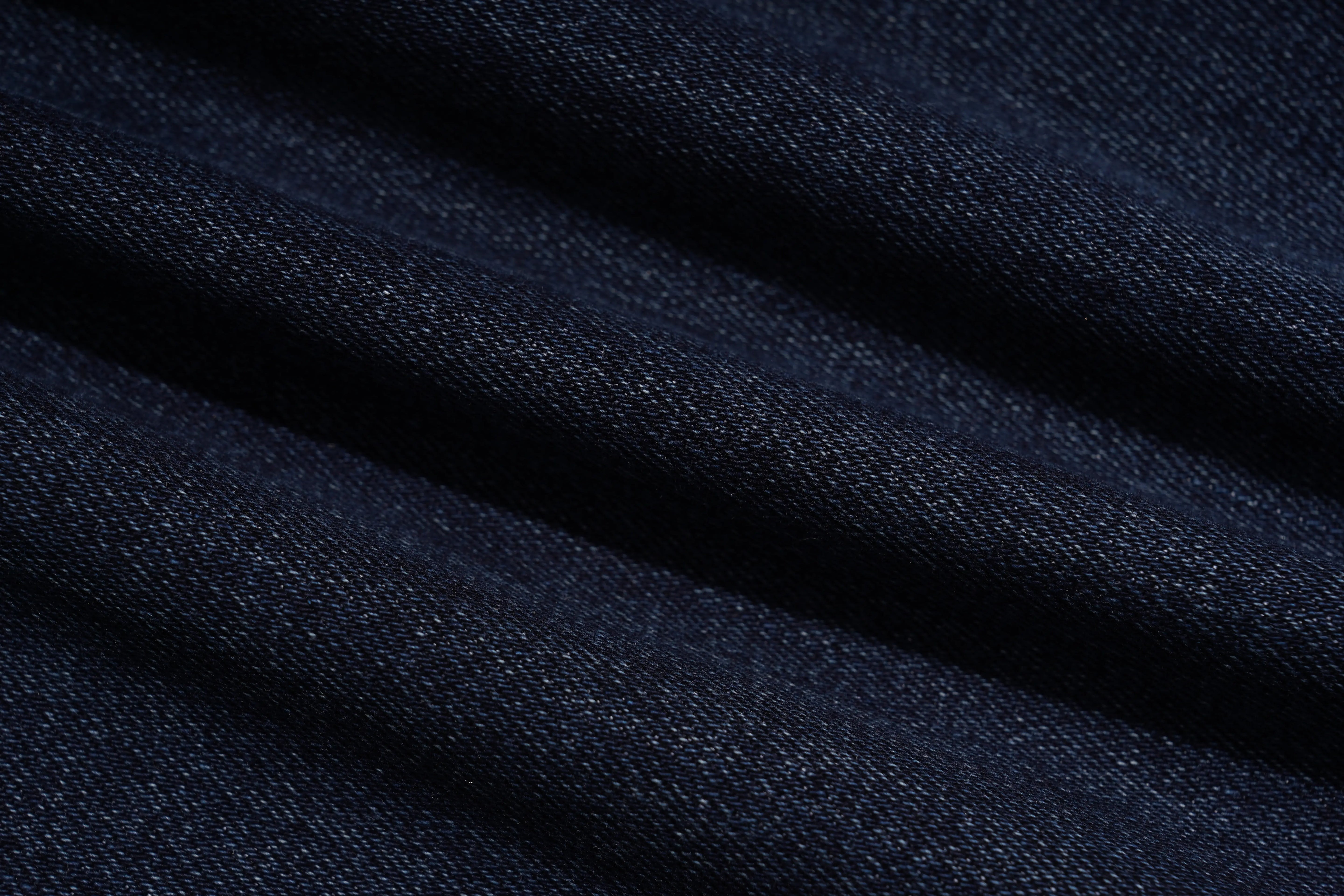 A close-up of dark navy blue textured fabric with soft diagonal folds and a fine woven pattern. TCH Rhinestone Shooting Star Galaxy Jeans
