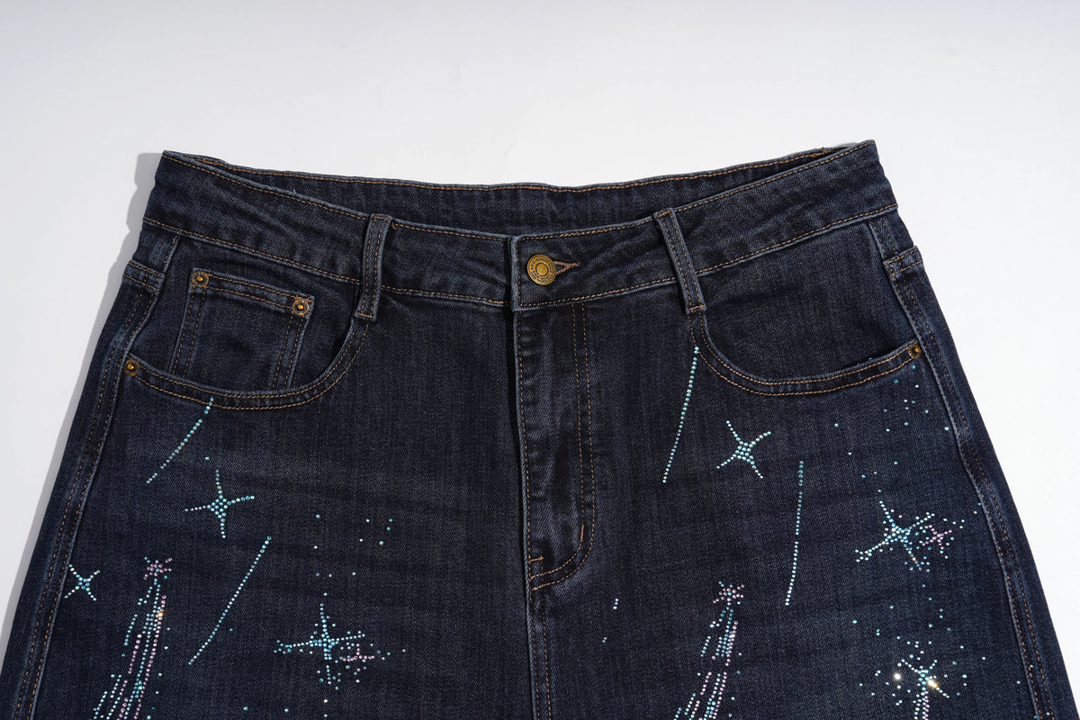 Dark indigo denim jeans featuring embroidered star and firework patterns in light blue and white thread, shown against a plain white background. TCH Rhinestone Shooting Star Galaxy Jeans