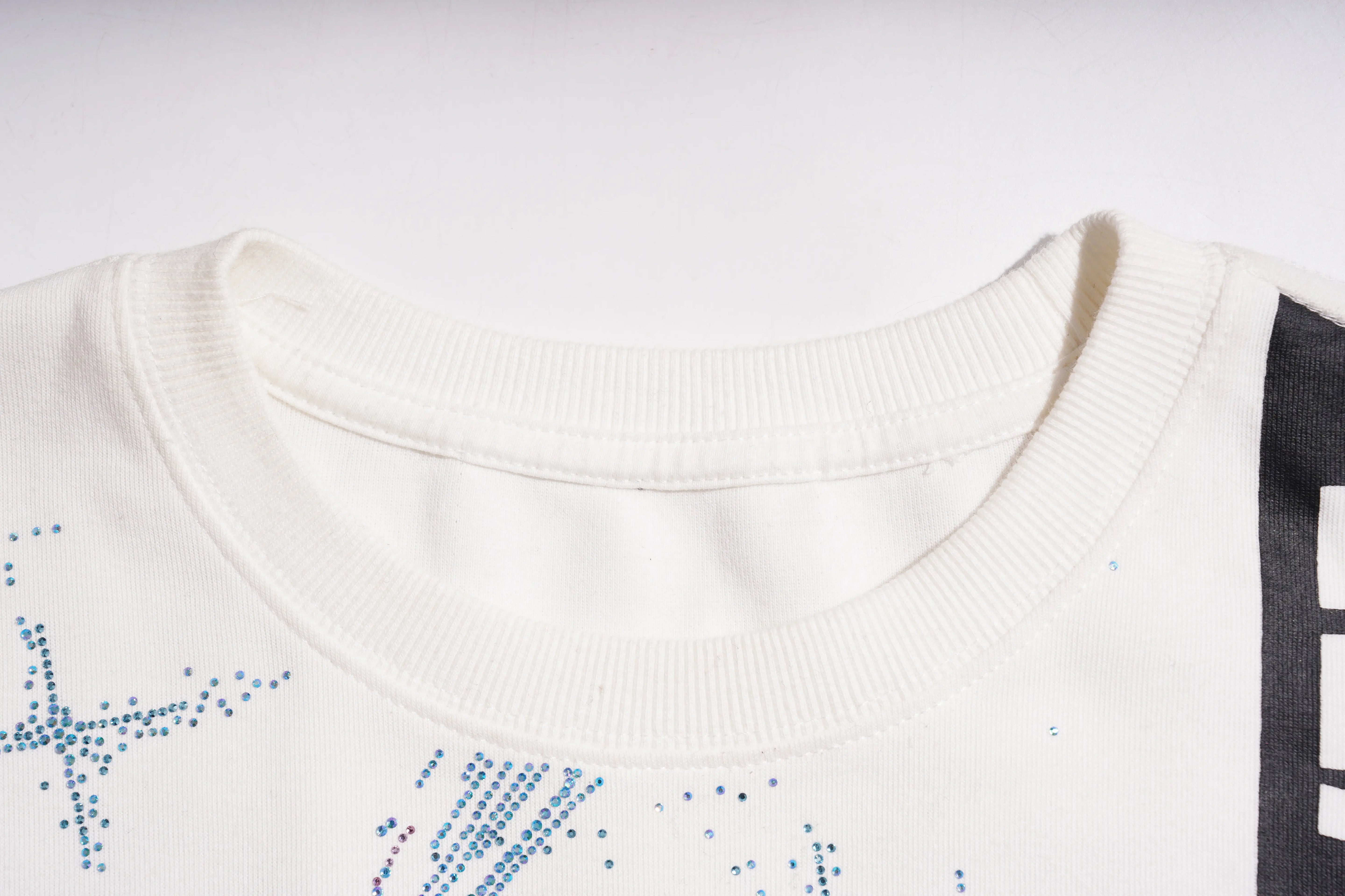 Close-up of a white garment with blue embellishments on a light gray background TCH Rhinestone Shooting Star Sweatshirt-