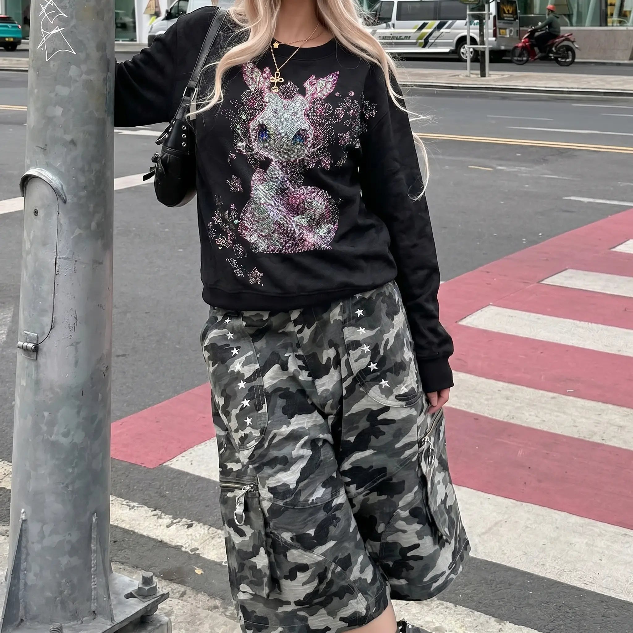 Person wearing a black sweatshirt with a floral design and camouflage pants on a city street. TCH Rhinestone Snake Black Crewneck Sweatshirt