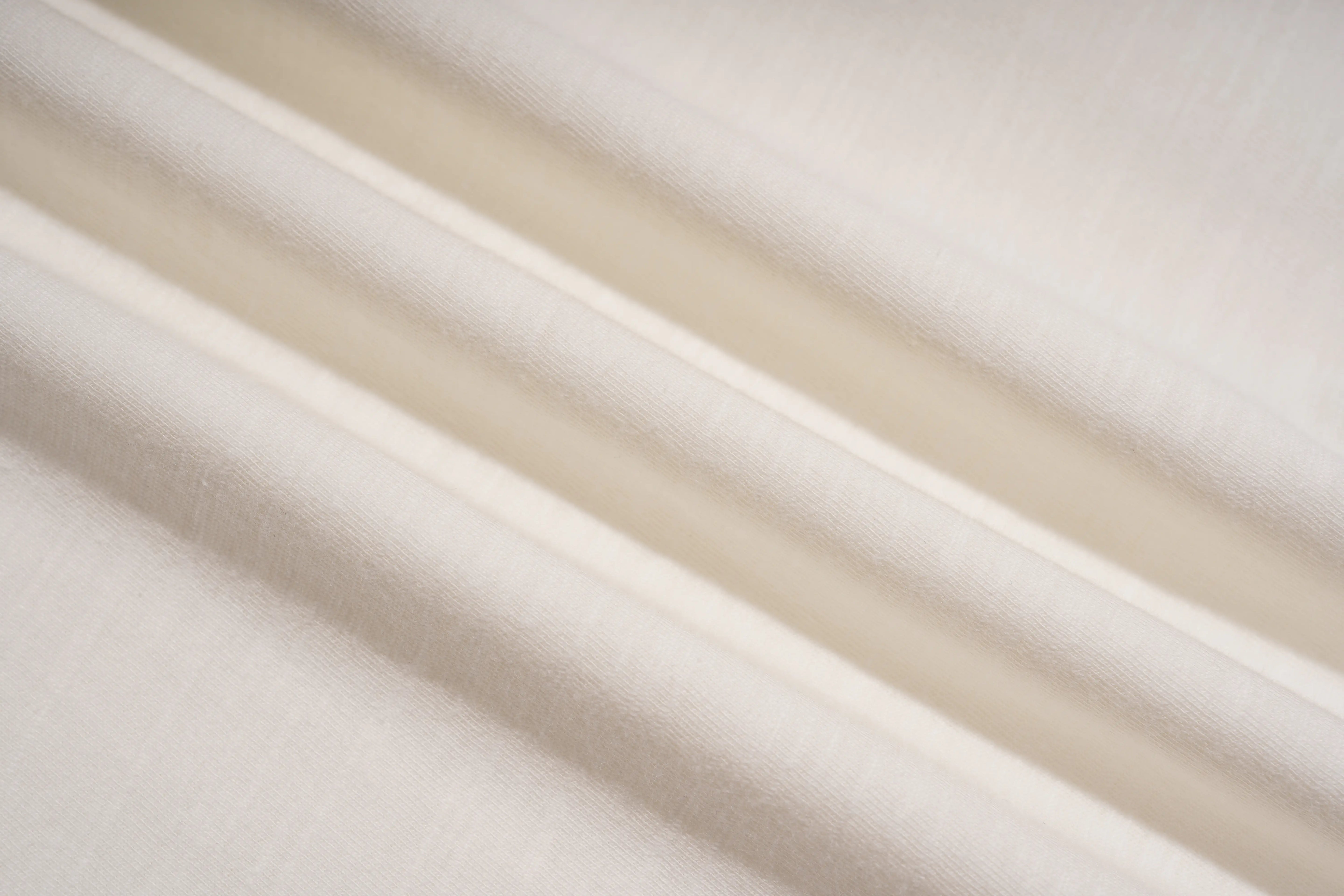 A close-up of draped off-white fabric with soft diagonal folds and a subtle woven texture. TCH Rhinestone Sparkle Crystal Graphic White T-Shirt
