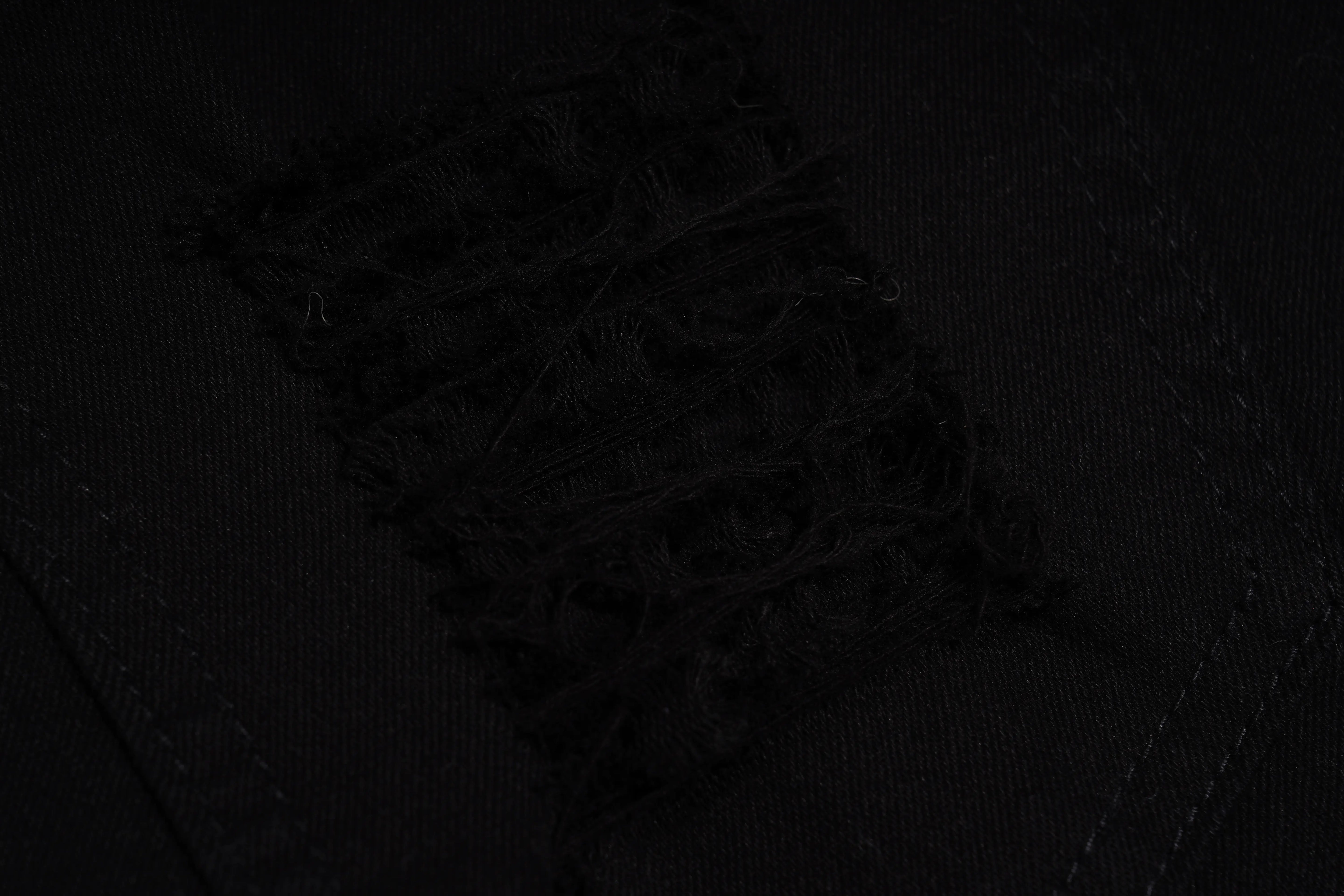 Close-up of a black fabric surface with a distressed, frayed rectangular patch and visible stitching. TCH Rhinestone Sunflower Distressed Denim Shorts