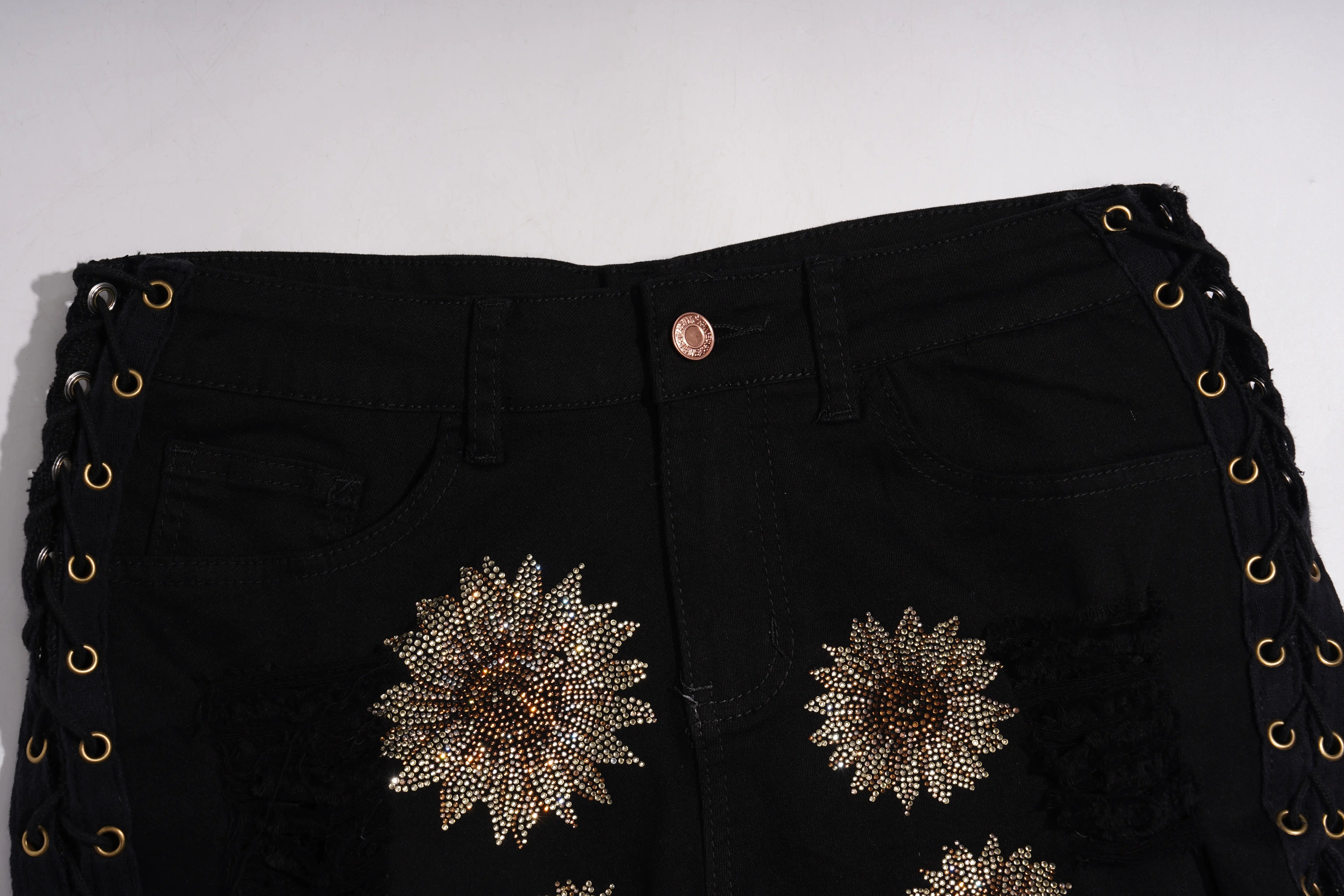 Black denim jeans featuring large, ornate gold and brown rhinestone sunflower patches on the front, with gold-tone grommet lace-up detailing along the sides. TCH Rhinestone Sunflower Distressed Denim Shorts