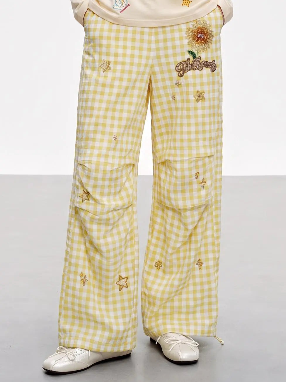 Yellow and white gingham wide-leg pants with embroidered sunflowers, stars, and a cursive 'Happiness' patch on the left thigh, shown on a model wearing white shoes. TCH Rhinestone Sunflower Gingham Cargo Wide-Leg Pants
