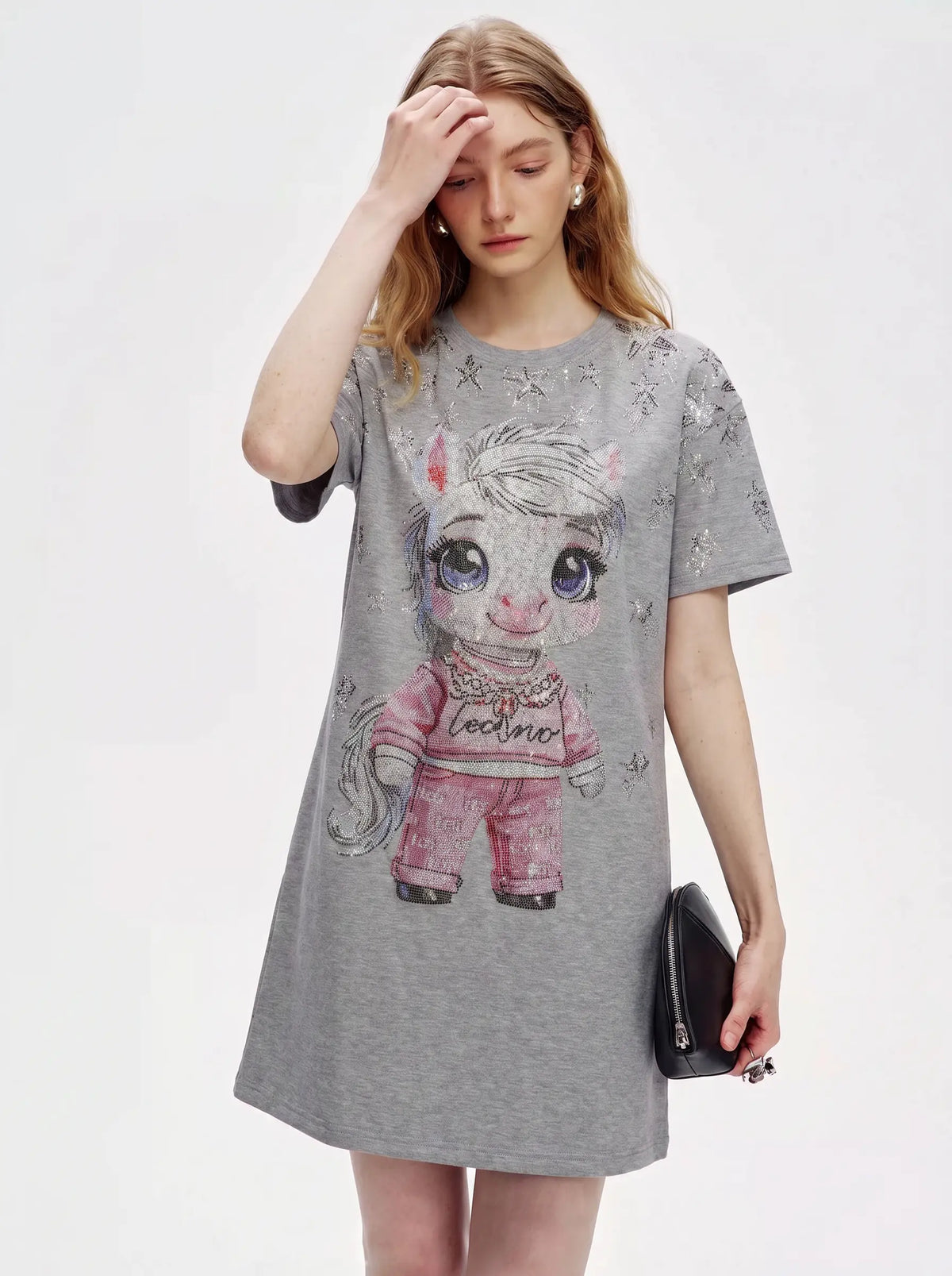 A woman modeling a heather gray short-sleeve t-shirt dress featuring a large cartoon pony graphic on the front, styled with a small black clutch against a plain white background. TCH Rhinestone Techno Unicorn Graphic T-Shirt