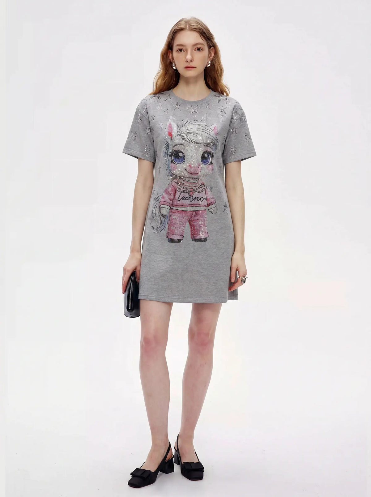 A woman modeling a gray short-sleeve mini dress with a cartoon pony graphic on the front, styled with black flats and holding a black clutch against a plain white studio background. TCH Rhinestone Techno Unicorn Graphic T-Shirt