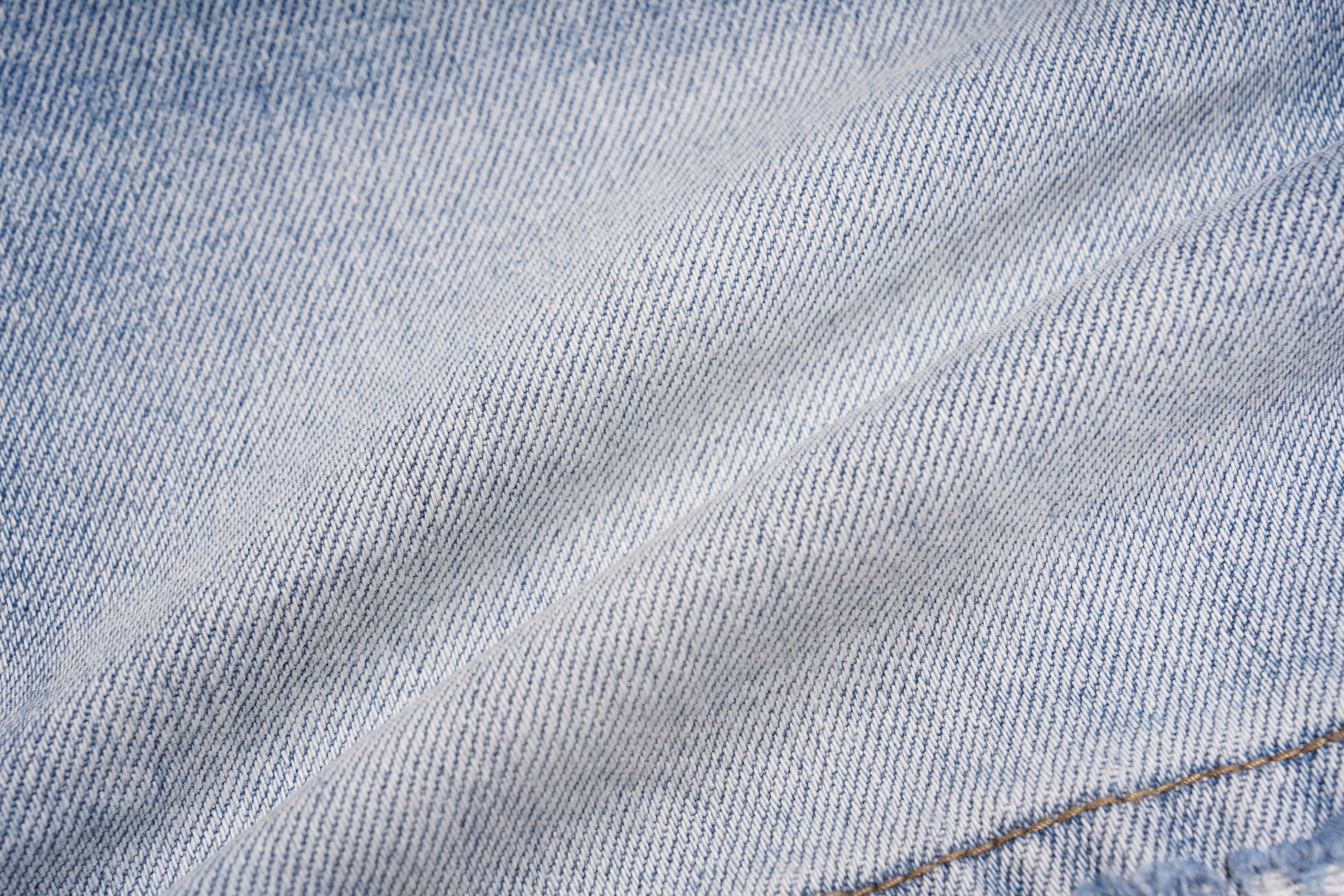 A close-up of light blue denim fabric with a diagonal twill weave and a small section of gold-colored stitching visible in the lower right corner. TCH Rhinestone Teddy Bear Bow Denim Shorts