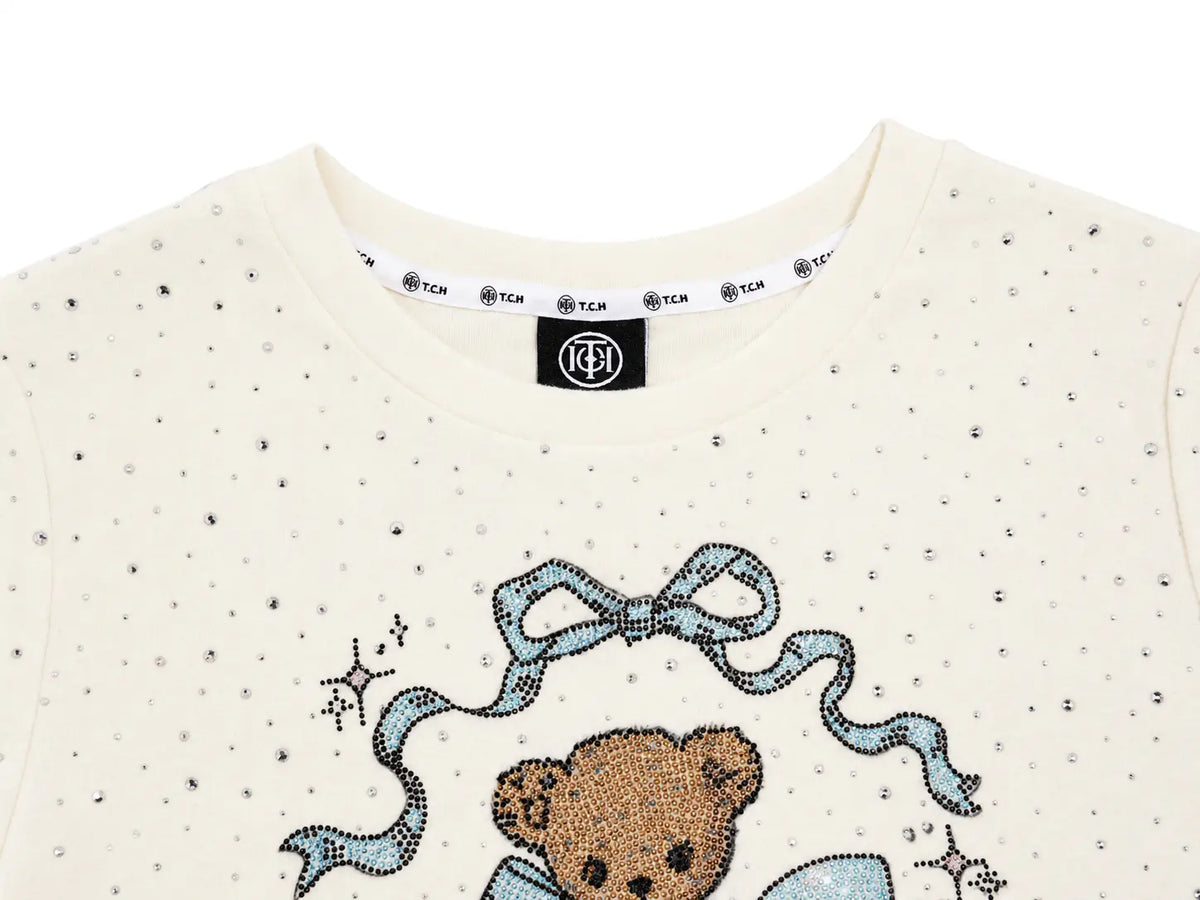 Close-up of a cream-colored TCHC sweatshirt featuring a rhinestone teddy bear graphic with a blue bow, on a white background. TCH Rhinestone Teddy Bear Bow Graphic Cropped T-Shirt