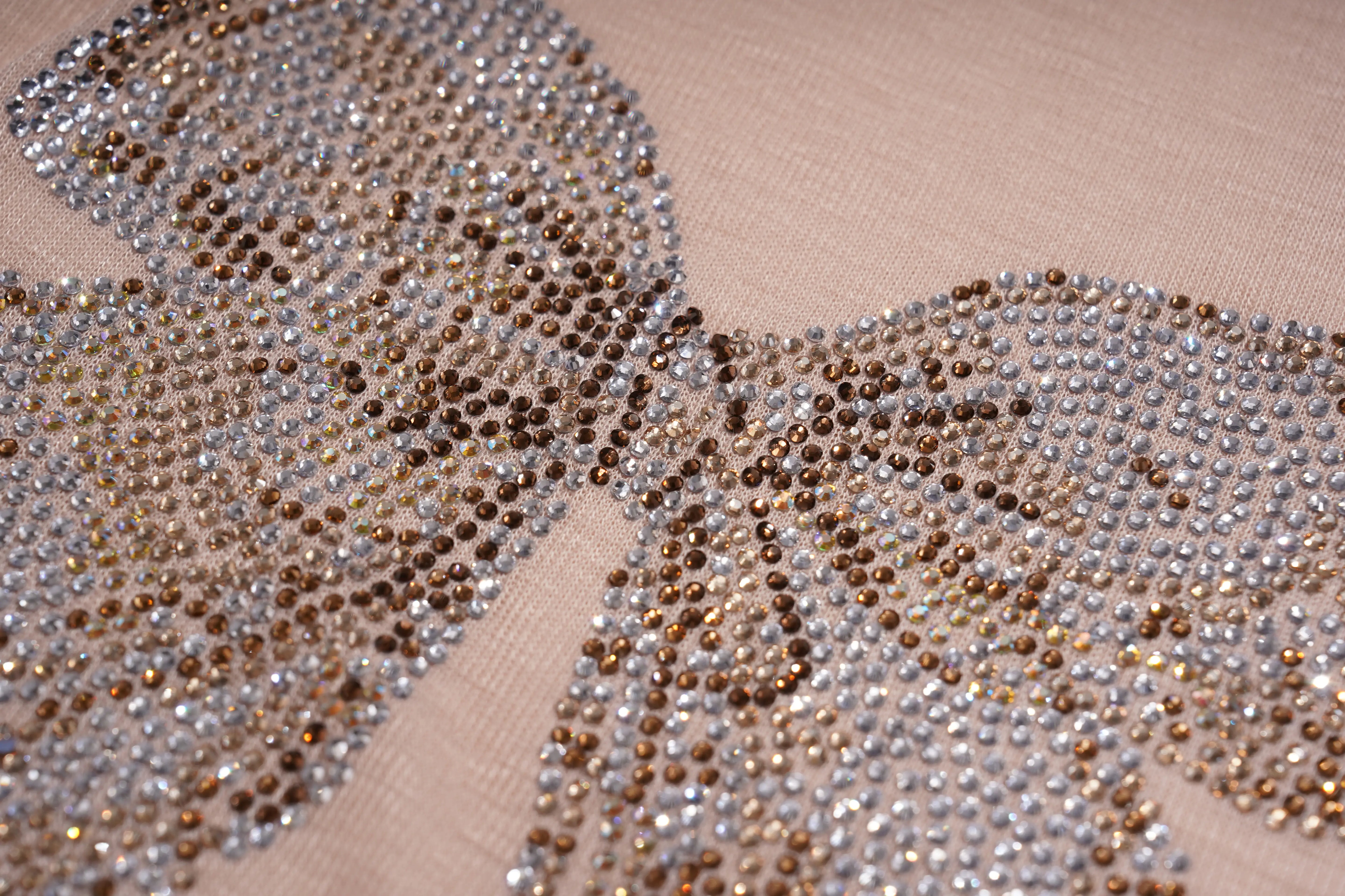 A close-up of a butterfly-shaped embellishment covered in clear rhinestones and small metallic gold and silver rhinestones, set against a beige fabric background. TCH Rhinestone Teddy Bear Bow Ruffle Long Sleeve Top