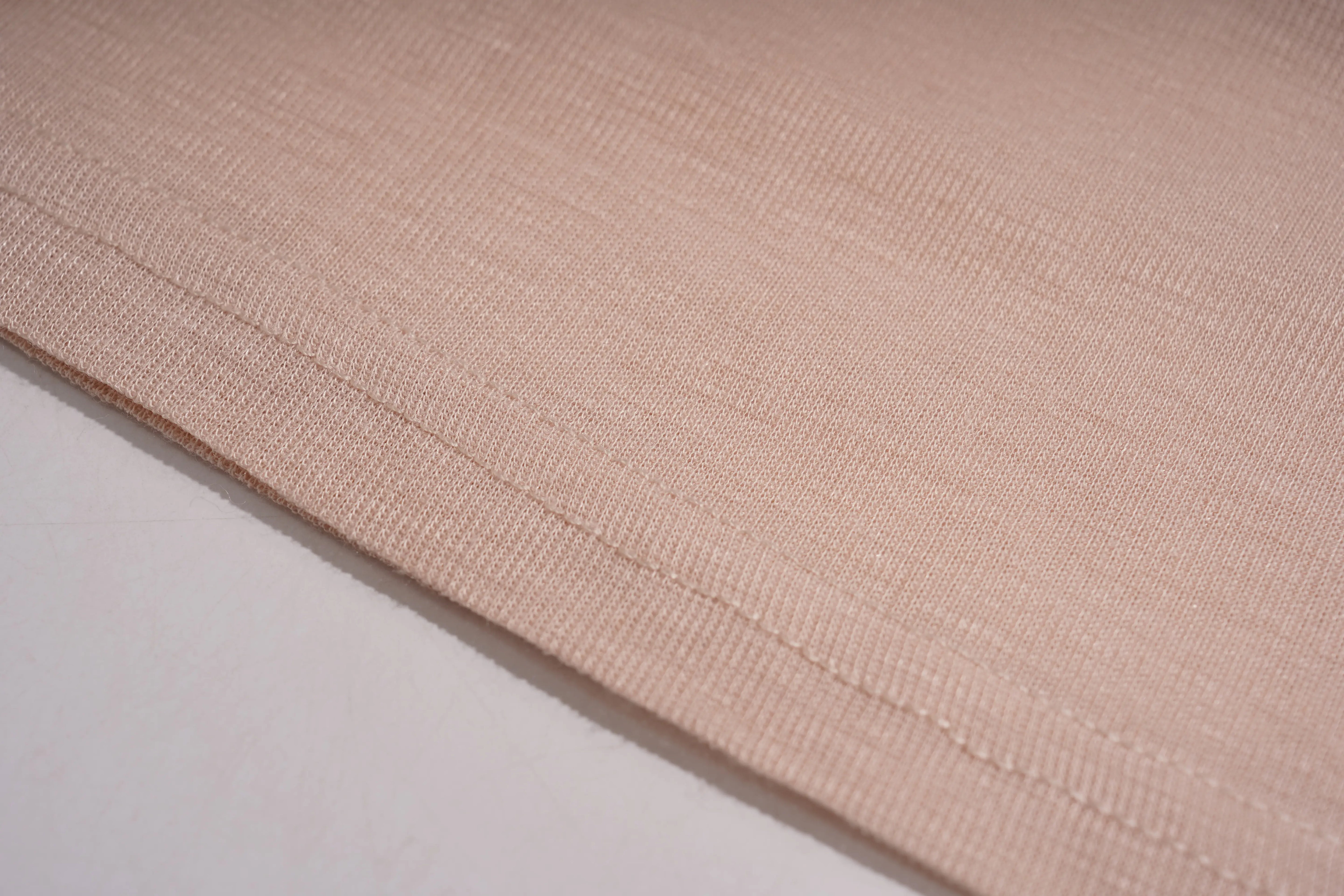 A close-up of a light beige or blush pink knit fabric with a fine ribbed texture and a neat hem, shown against a plain white background. TCH Rhinestone Teddy Bear Bow Ruffle Long Sleeve Top
