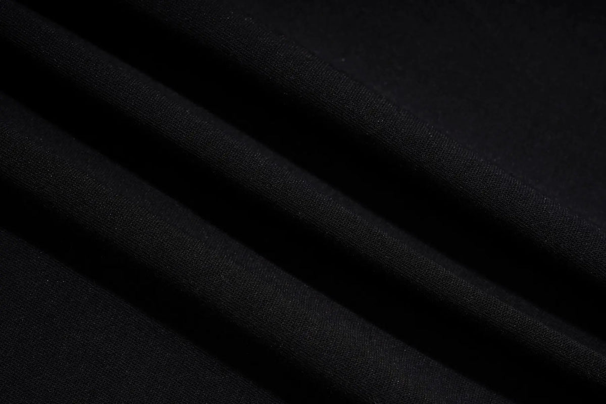 A close-up of draped black fabric with soft diagonal folds and a smooth matte texture. TCH Rhinestone Teddy Bear Cherry Graphic Sweat Shorts