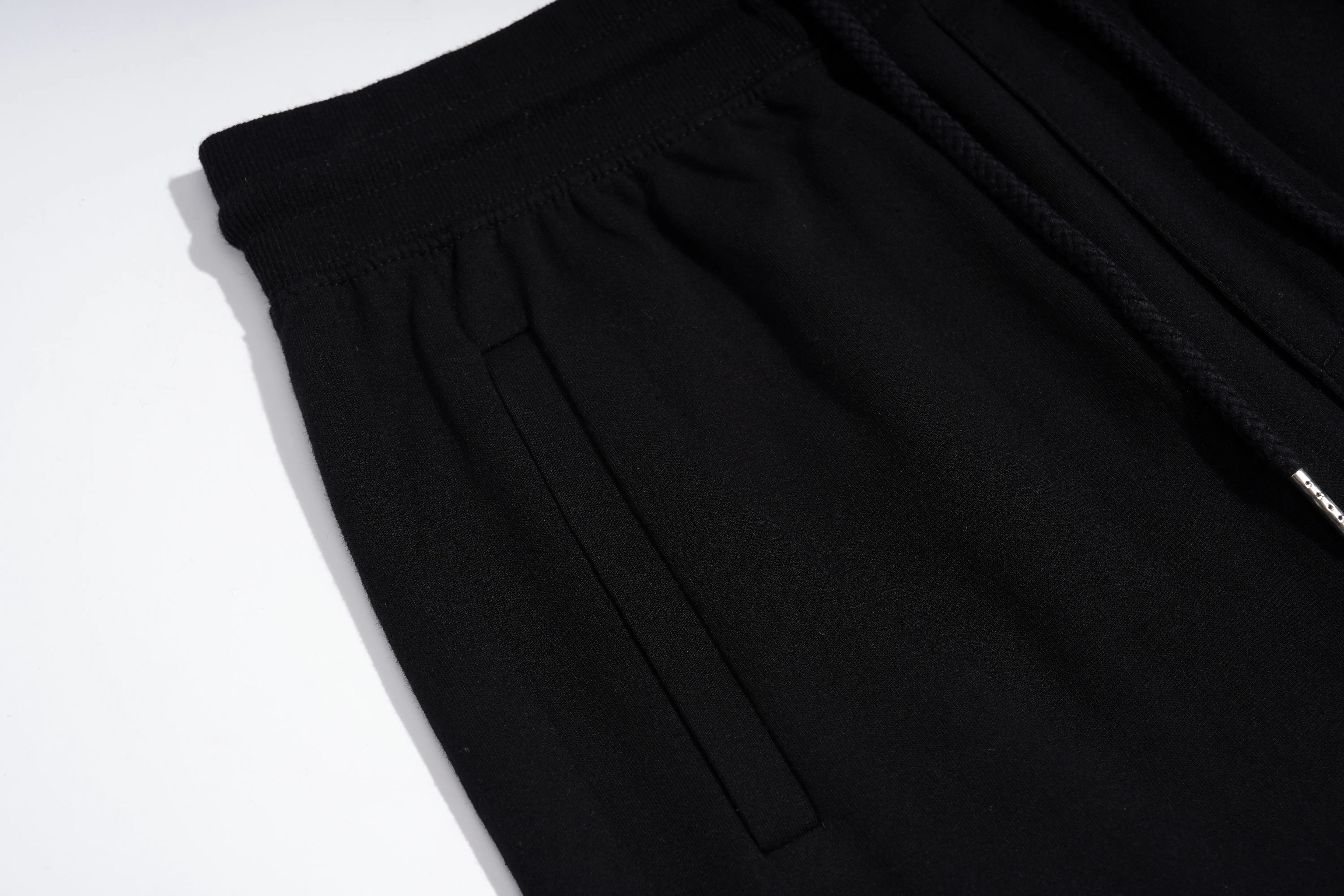 Close-up of black drawstring pants showing the elastic waistband, side pocket seam, and a black drawstring with a small silver metal tip on a white background. TCH Rhinestone Teddy Bear Graphic Black Jogger Pants