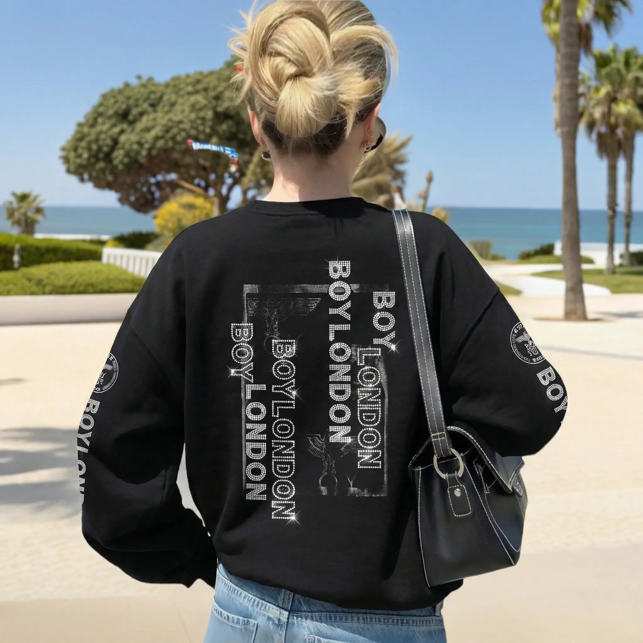 Person wearing a black sweatshirt with 'Boy London' branding, standing by a beach. TCH Rhinestone Teddy Bear Graphic Crewneck Sweatshirt-