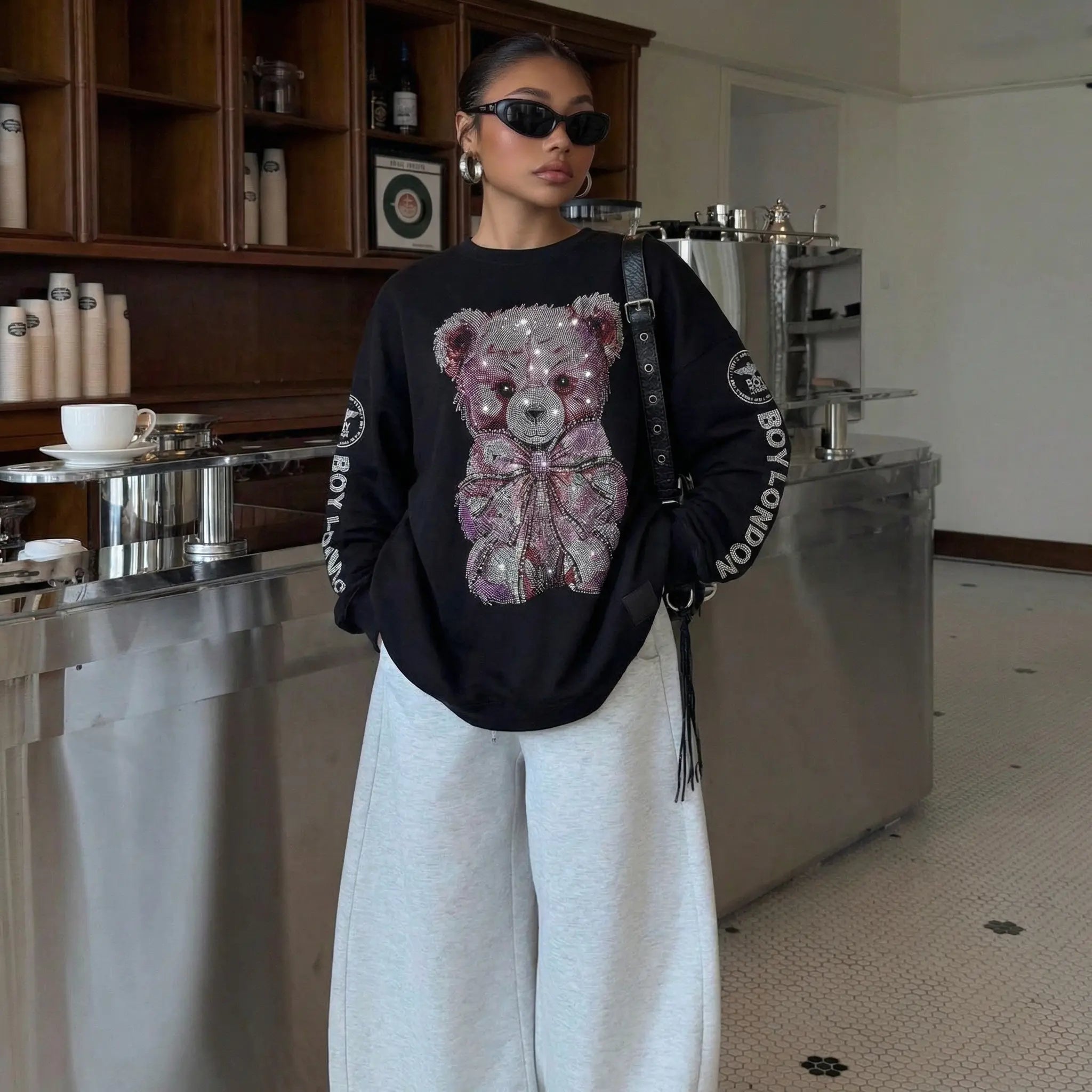 Person wearing a black sweater with a teddy bear design in a kitchen setting TCH Rhinestone Teddy Bear Graphic Crewneck Sweatshirt-