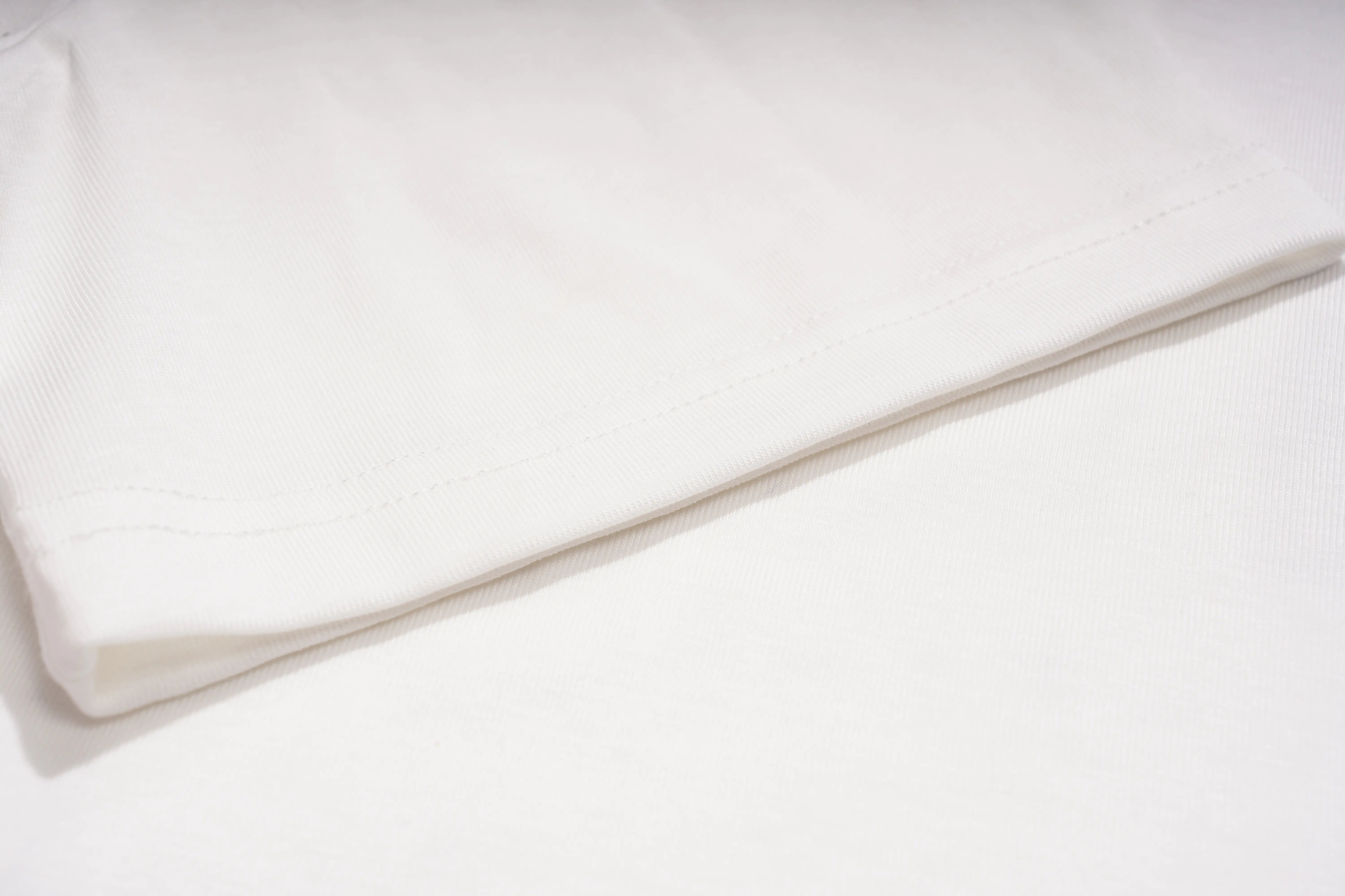 A close-up of a folded white fabric item, showing a clean stitched edge and soft texture against a matching white background. TCH Rhinestone Teddy Bear Lace Hooded T-Shirt